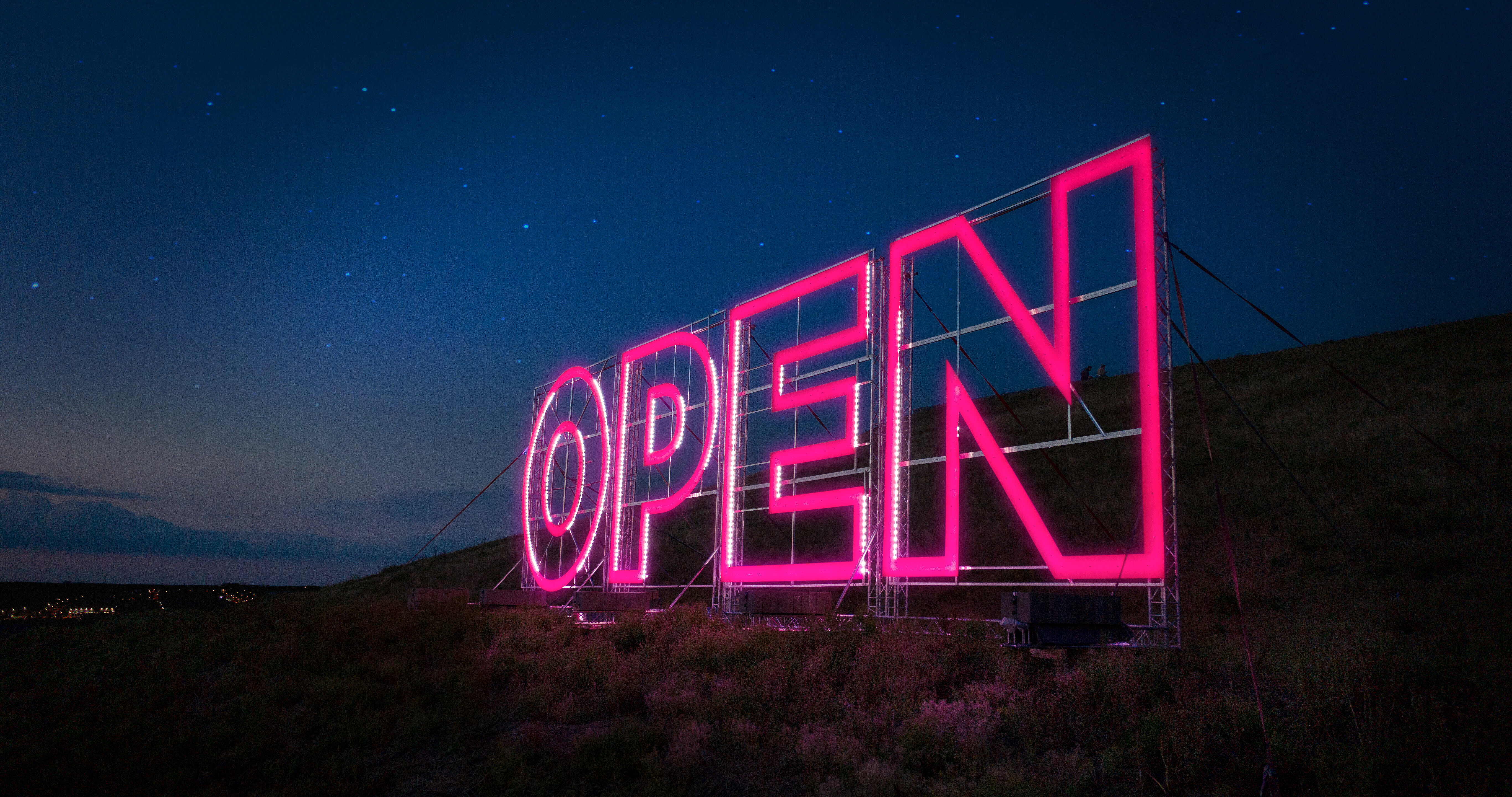 Pinker Leuchtschriftaufsteller mit dem Titel "OPEN", umgeben von Dunkelheit