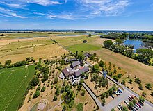 Blick von oben auf das RVR-Naturforum Bislicher Insel. Im Hintergrund sind Felder und der Rhein zu sehen.