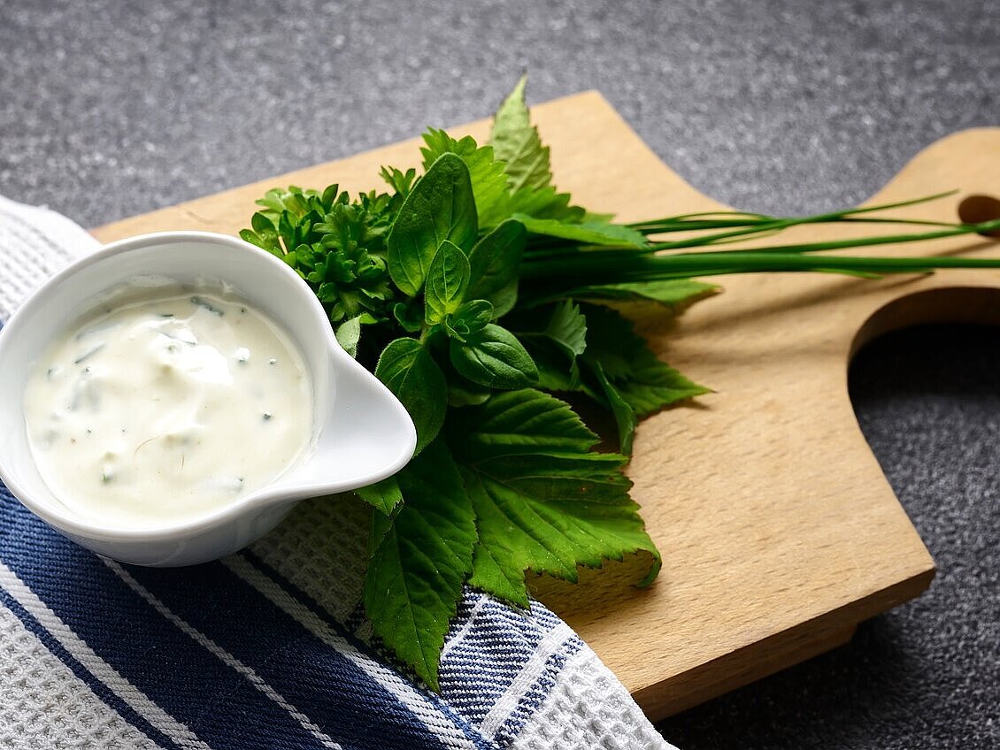 Eine Schüssel gefüllt mit Salatdressing, daneben liegen Kräuter. Beides wurde auf einem Holzbrett angerichtet.