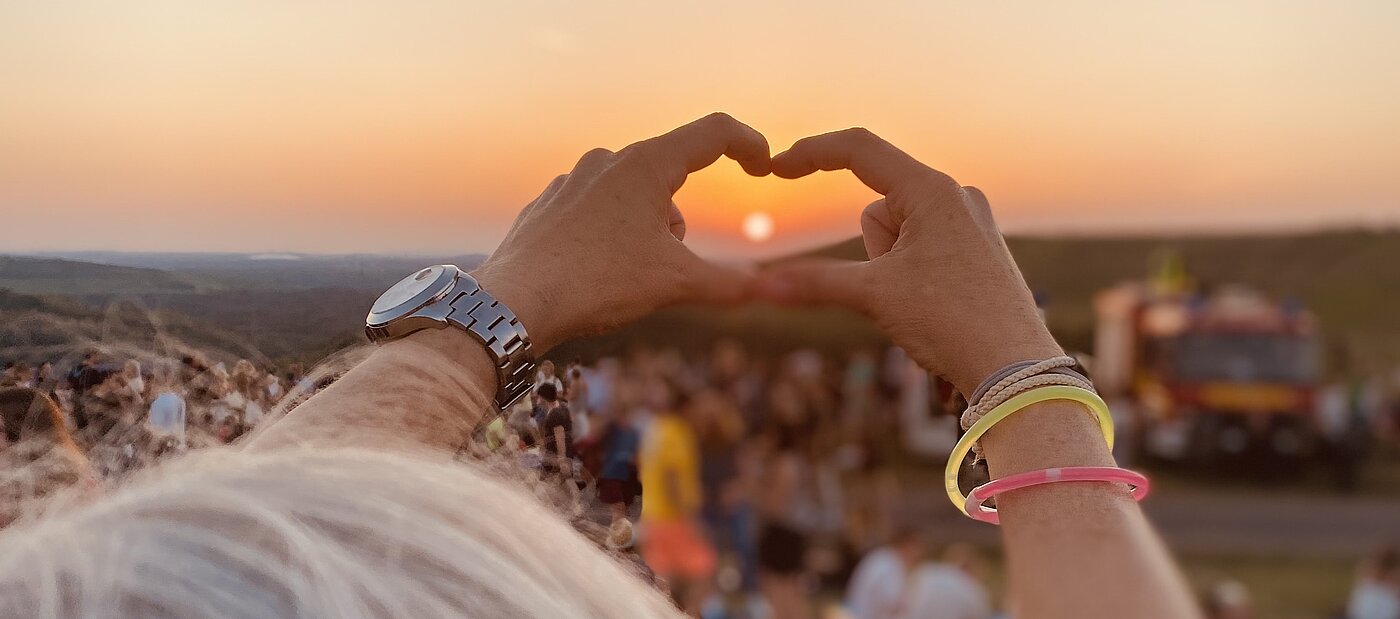 Sonnenuntergang auf der Halde Hoheward. Eine Hand formt ein Herz in Richtung Sonne. 