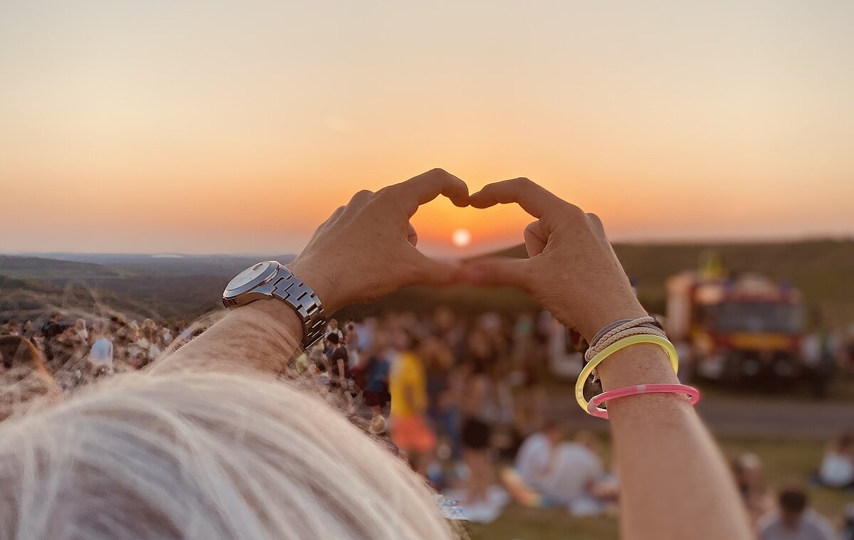 Sonnenuntergang auf der Halde Hoheward. Eine Hand formt ein Herz in Richtung Sonne. 