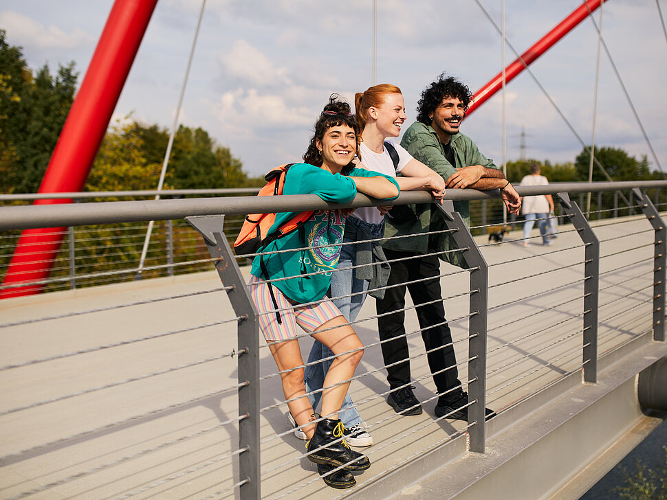 drei junge Menschen stehen auf einer Brücke, angelehnt an das Geländer