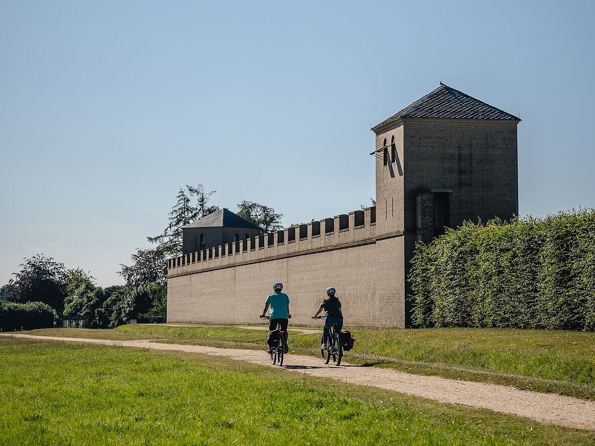Radfahrende entlang einer alten Mauer mit Turm.