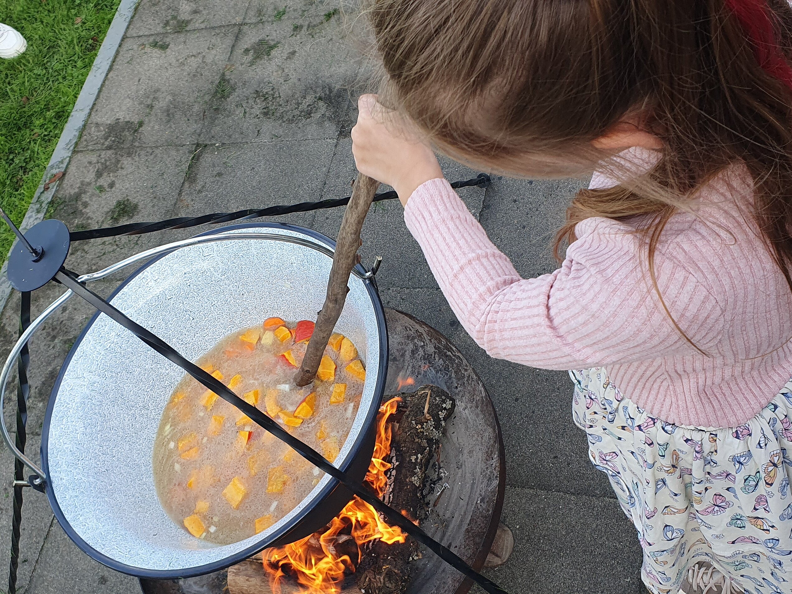 Ein Mädchen rührt in einem großen Topf mit Essen über dem Koffer