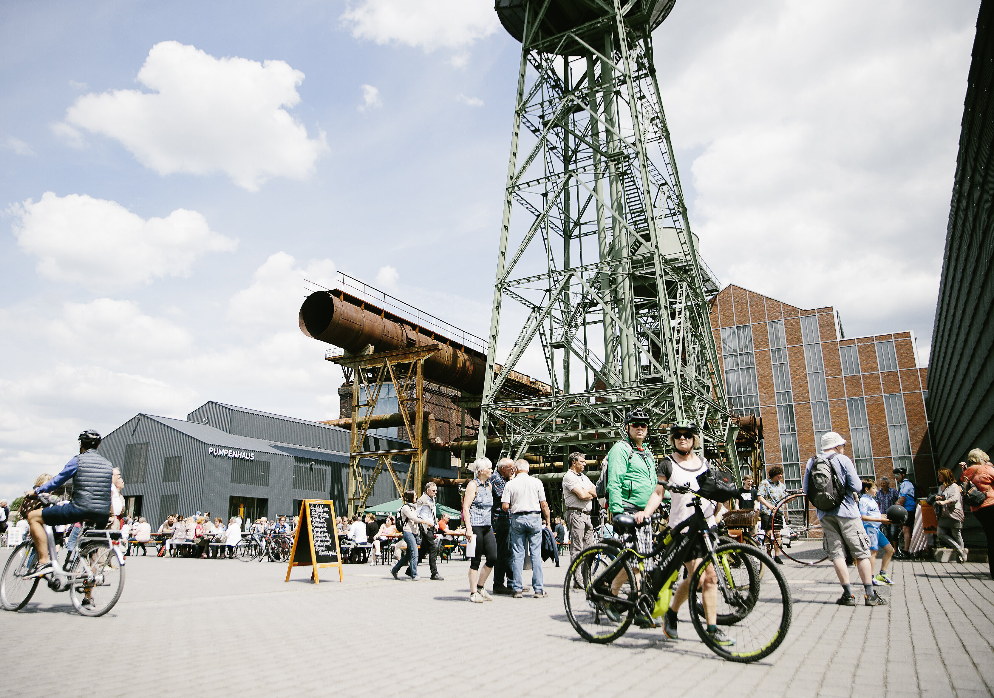 Im Vordergrund zwei Radfahrer, im Hintergrund die Jahrhunderthalle Bochum.