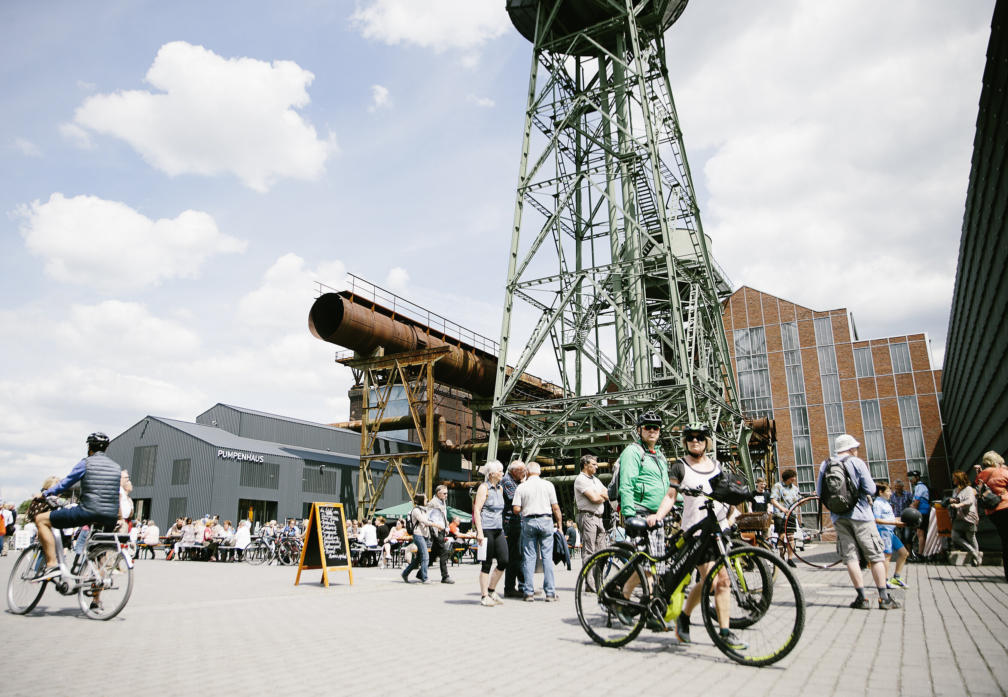 Im Vordergrund zwei Radfahrer, im Hintergrund die Jahrhunderthalle Bochum.