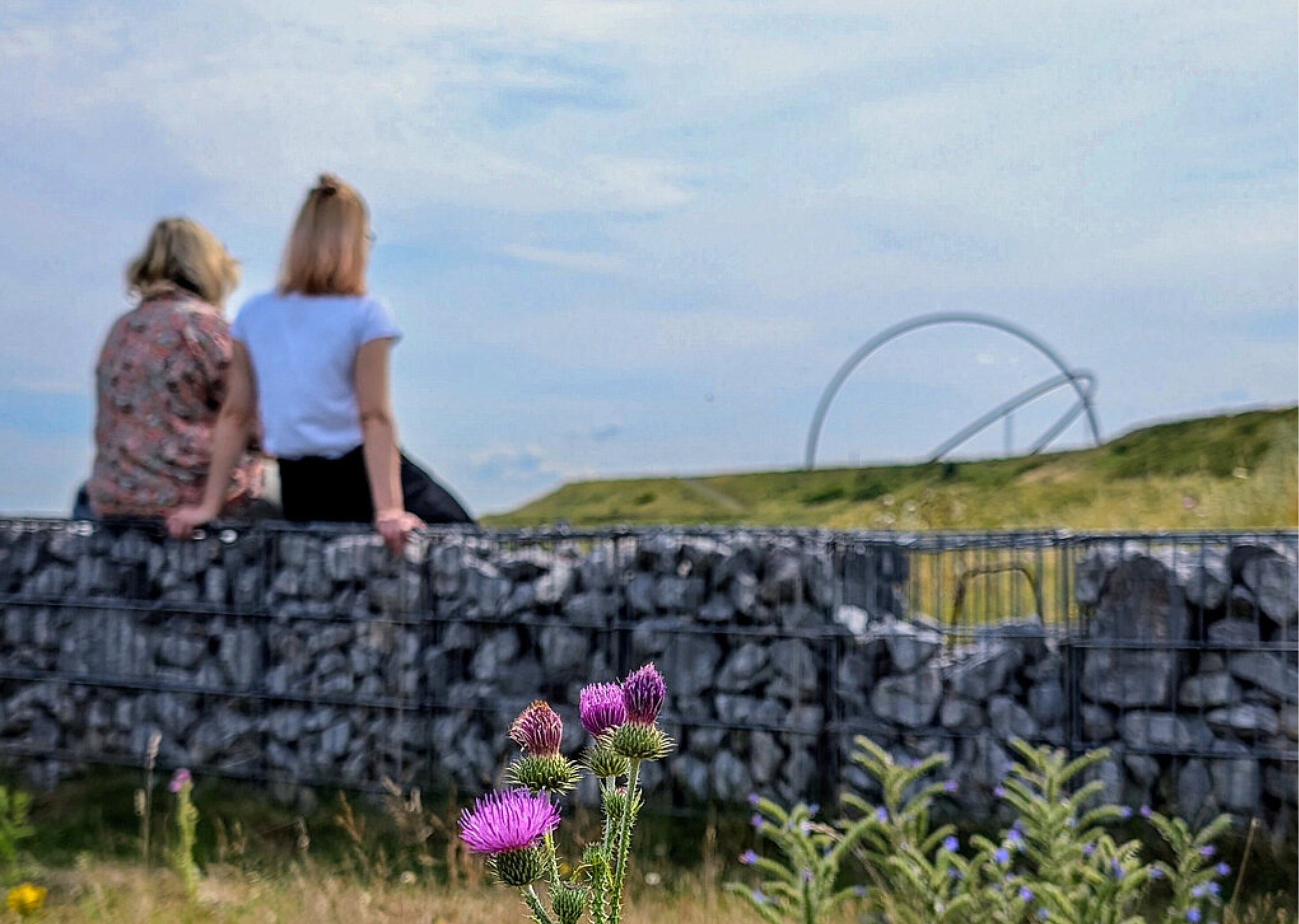 Zwei Personen sitzen auf einer Mauer und Blicken auf den Gipfel der Halde Hoheward.