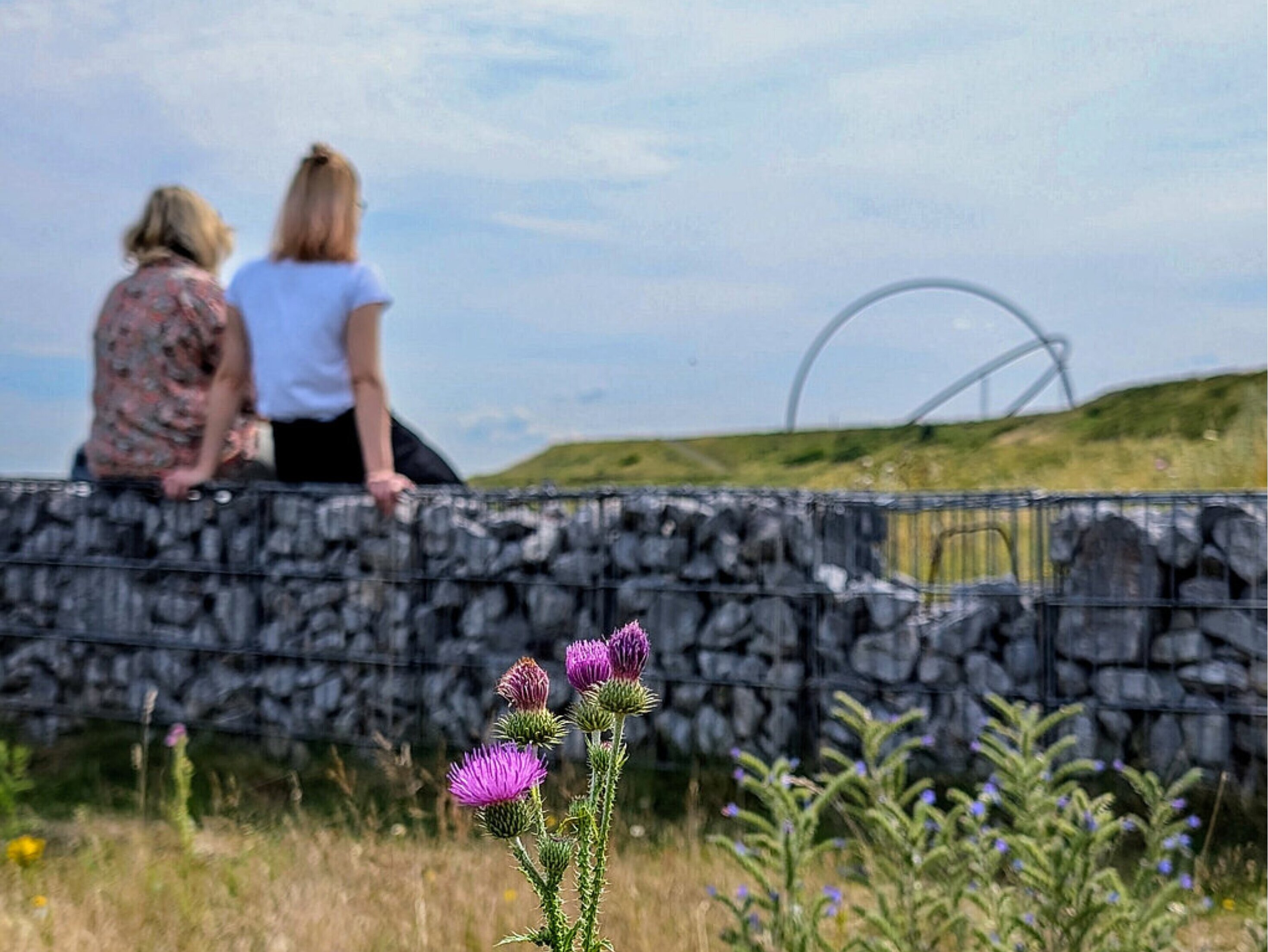 Zwei Personen sitzen auf einer Mauer und Blicken auf den Gipfel der Halde Hoheward.