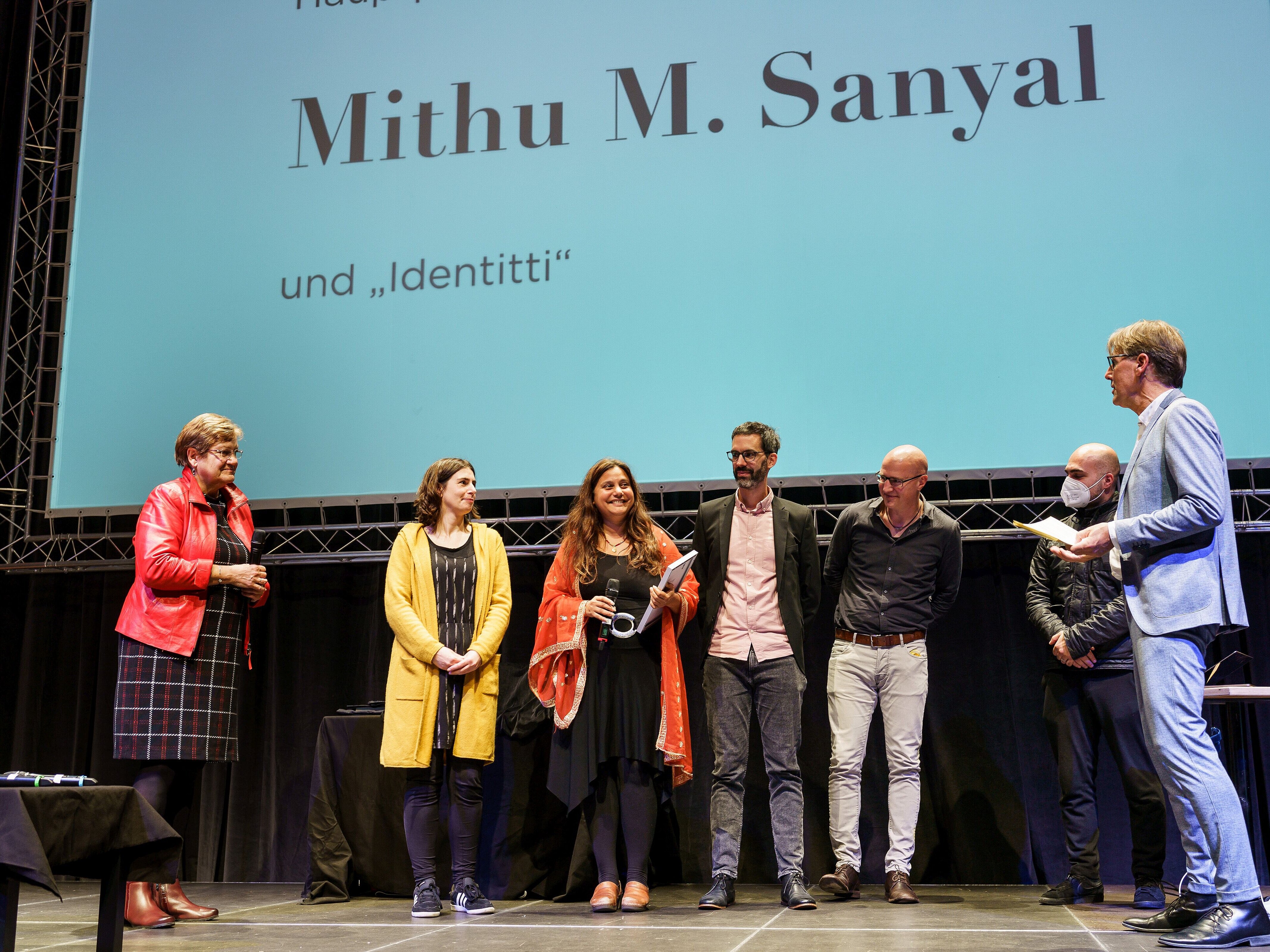 Hauptpreisträgerin Mithu M. Sanyal (Mitte) zusammen mit RVR-Regionaldirektorin Karola Geiß-Netthöfel (l.), Moderator Peter Großmann (r.) auf der Bühne im Ruhrfestspielhaus in Recklinghausen, begleitet von den weiteren Nominierten zum Hauptpreis des Literaturpreises Ruhr 2021.