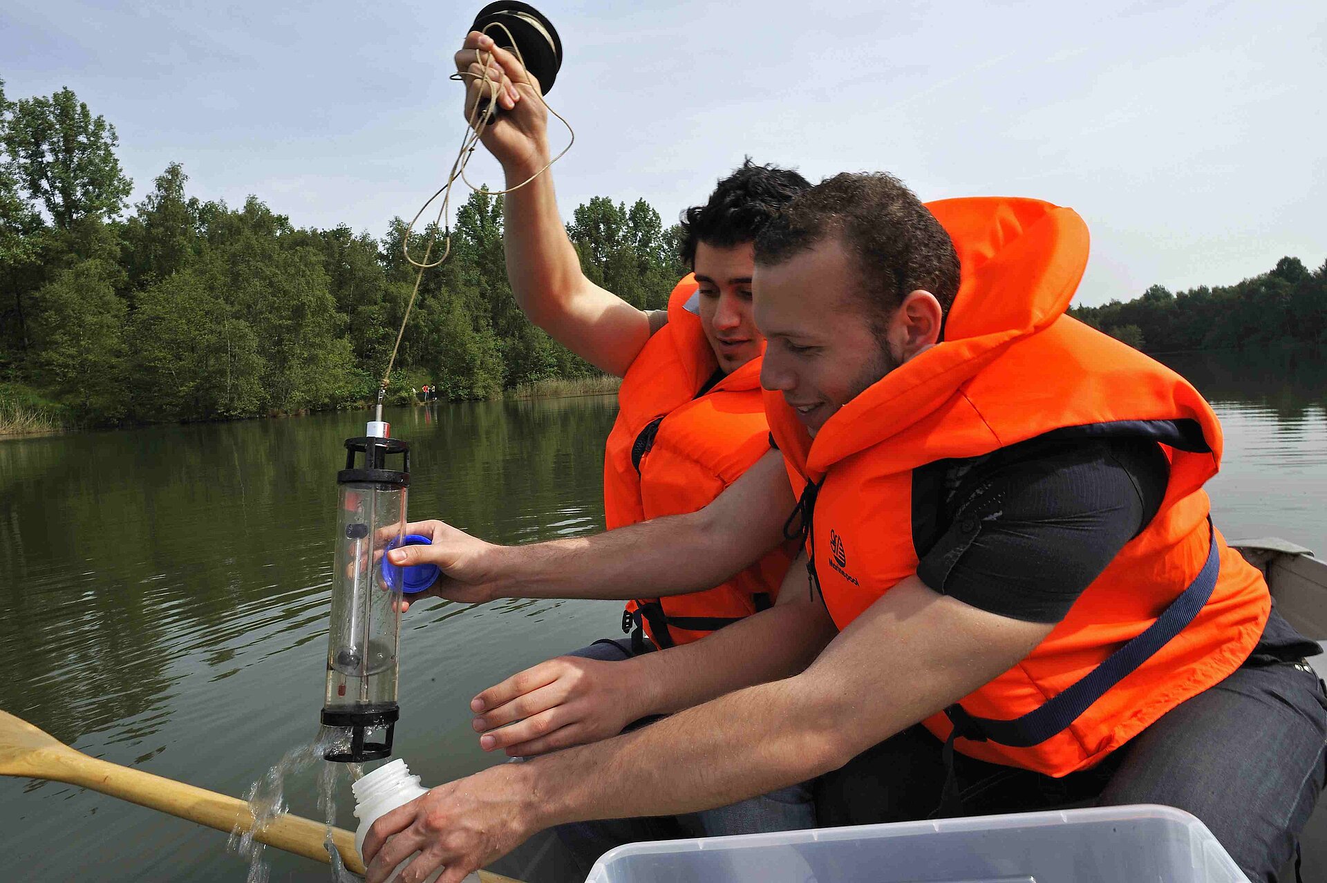 Zwei Schüler in Schwimmwesten sitzen in einem Boot und entnehmen Gewässerproben