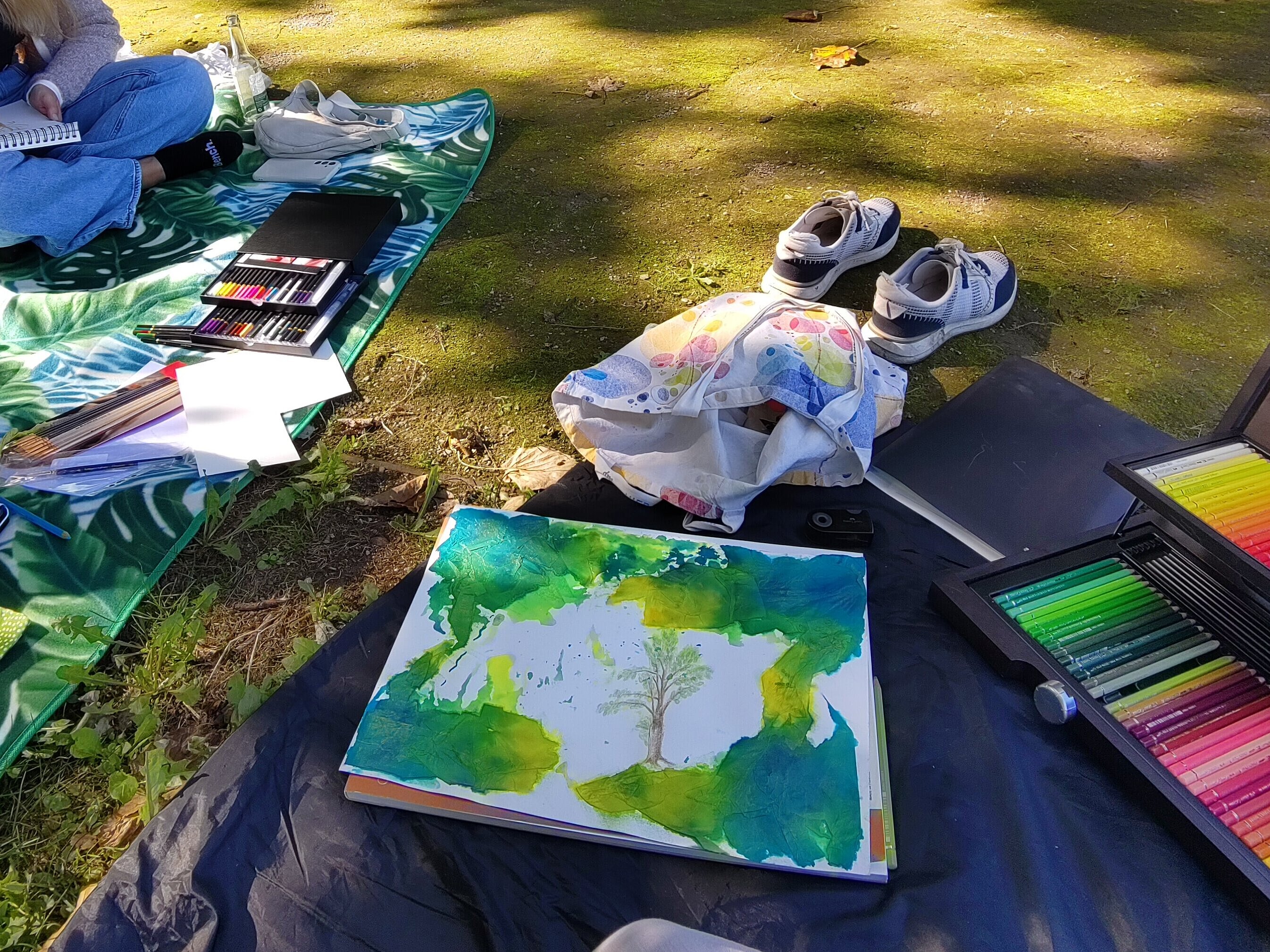 Es wird draußen auf einer Picknickdecke mit bunten Farben gemalt.