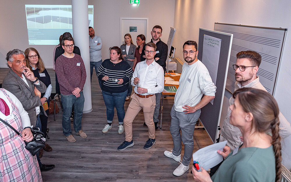 Personen stehen im Halbkreis vor einer Flipchart und reden miteinander