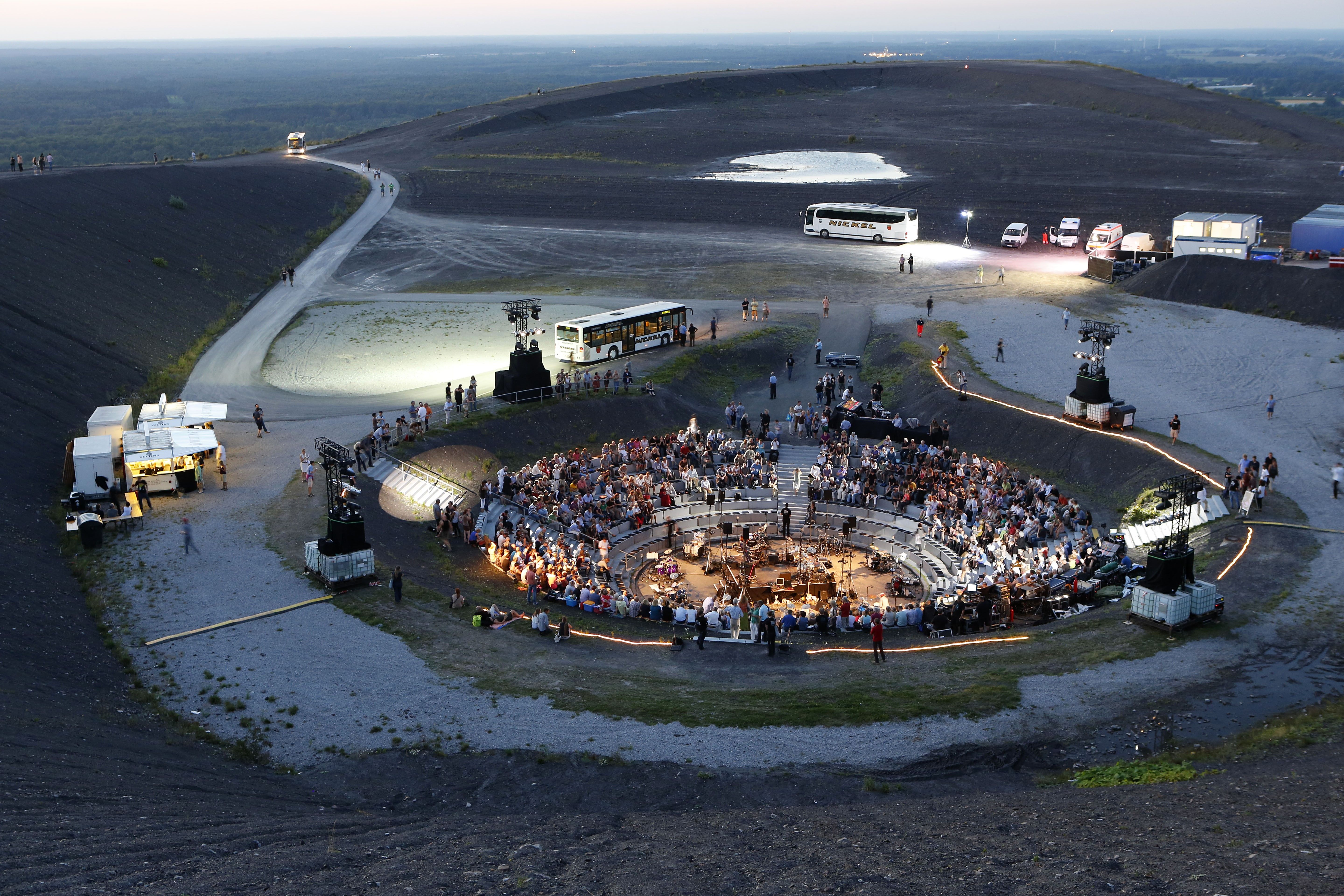 Menschen sitzen in der Abenddämmerung im Amphitheater auf dem Gipfelplateau der Halde.