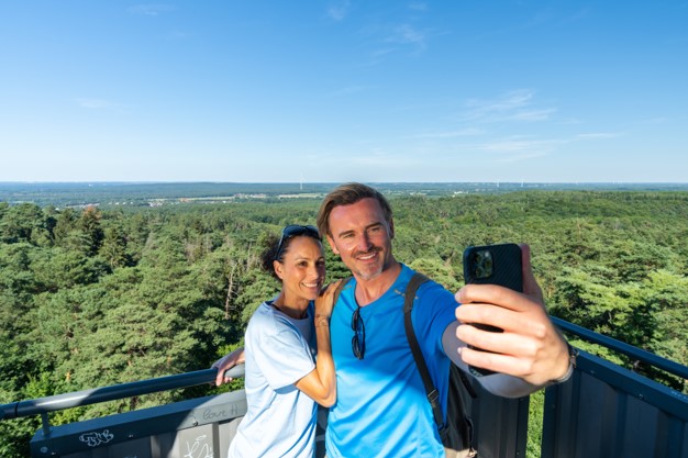 ein Pärchen macht ein Selfie von einem Feuerwachturm in Richtung Wald