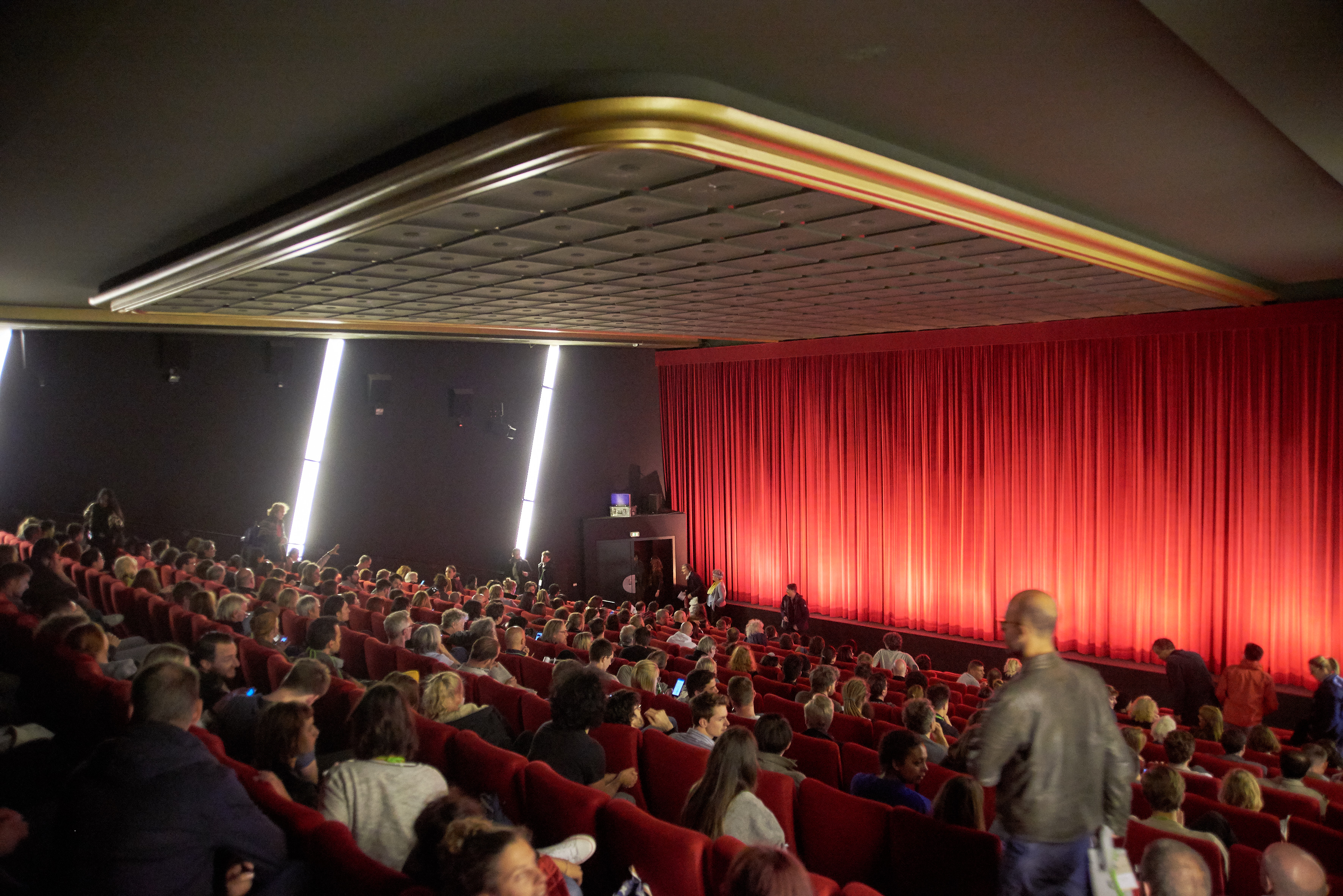 Voller Saal im Lichtburg Filmpalast. Menschen nehmen gerade Platz. Im Hintergrund ein roter Vorhang. 