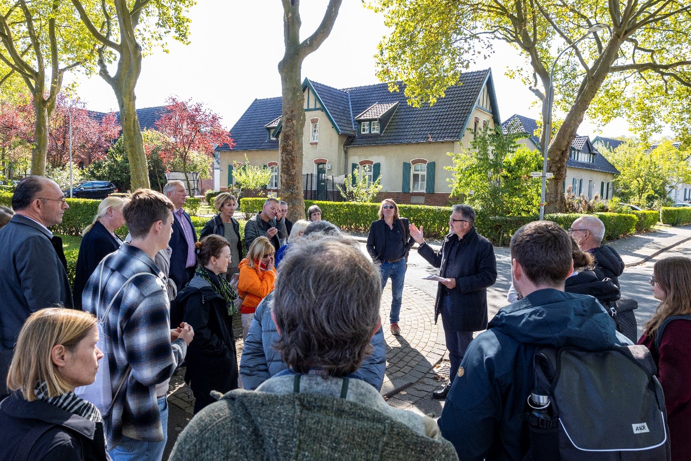Gruppe von Menschen stehen unter einem Baum. Mann erklärt was der Gruppe.