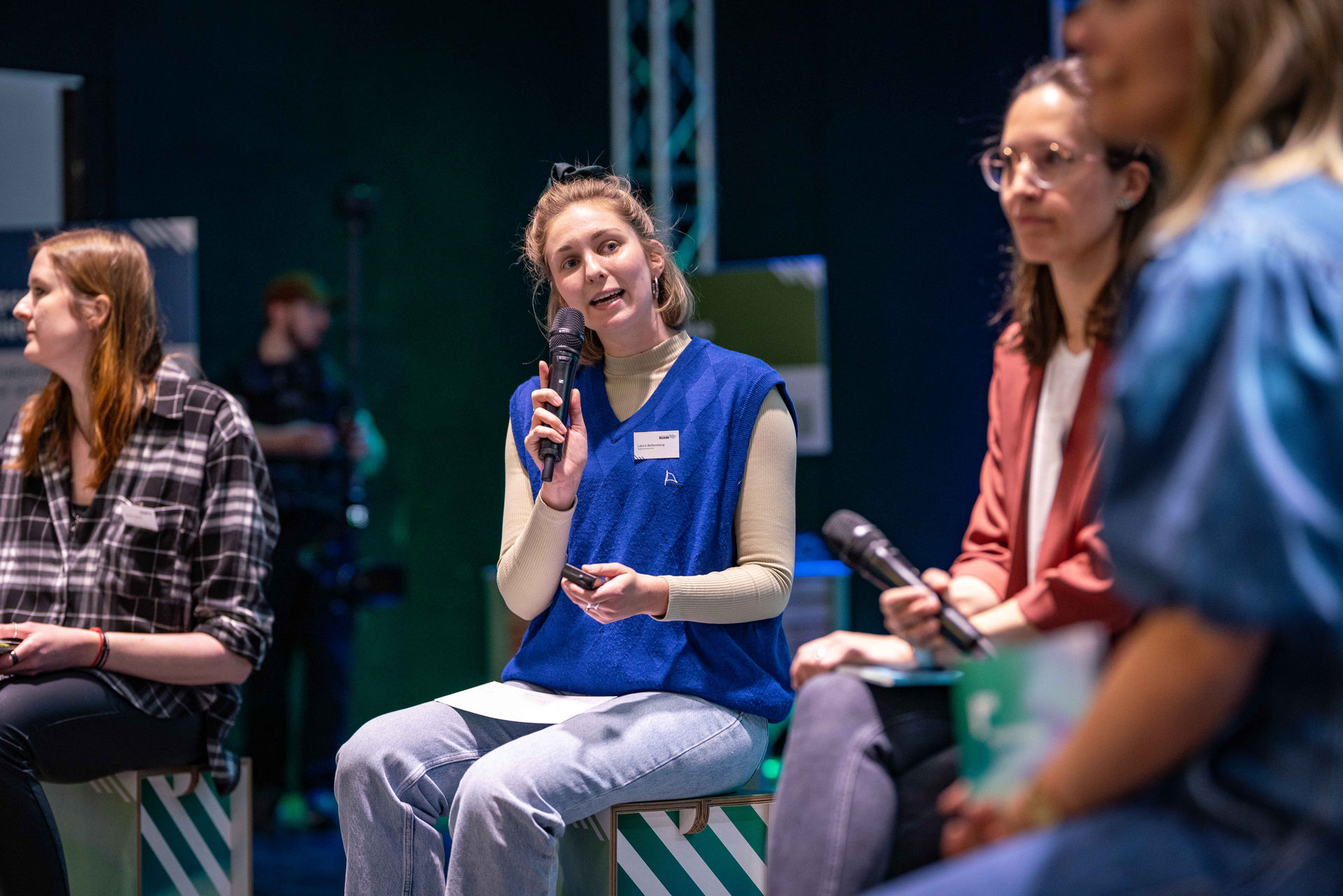 Laura Bellenberg, zuständig für Kommunikation und Veranstaltungen im Team Grüne Infrastruktur und Klimaneutralität im Referat Klima und Umweltschutz des Regionalverbands Ruhr, sitzt auf der Bühne des Netzwerktags Grüne Infrastruktur und hält ein Mikrofon in der Hand.