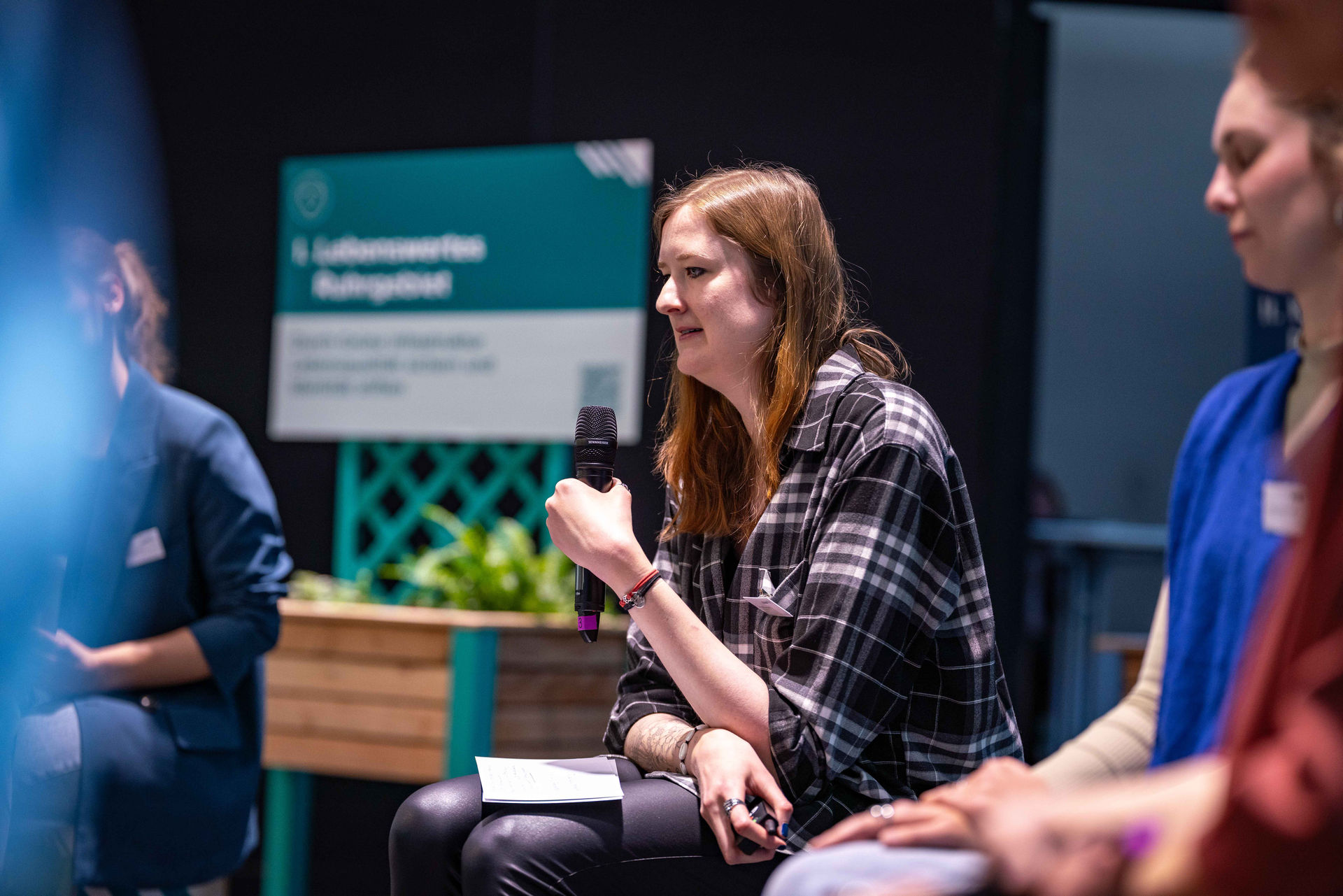 Leonie Krelaus, zuständig für digitale Tools  im Team Klimaanpassung im Referat Klima und Umweltschutz des Regionalverbands Ruhr, sitzt auf der Bühne des Netzwerktags Grüne Infrastruktur und hält ein Mikrofon in der Hand.