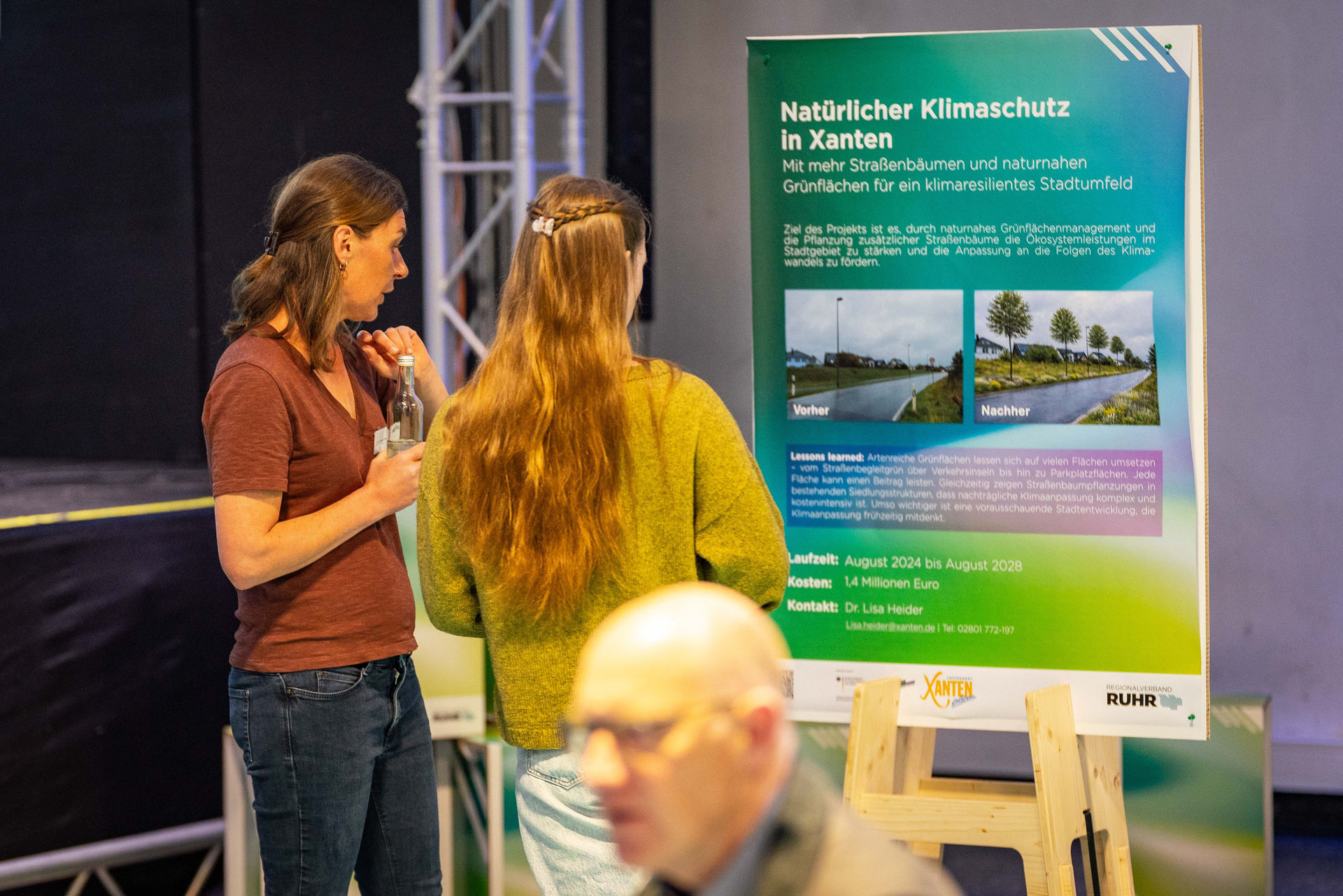 Dr. Lisa Heider steht vor einem Plakat der Stadt Xanten und disuktietr mit Teilnehmerin.