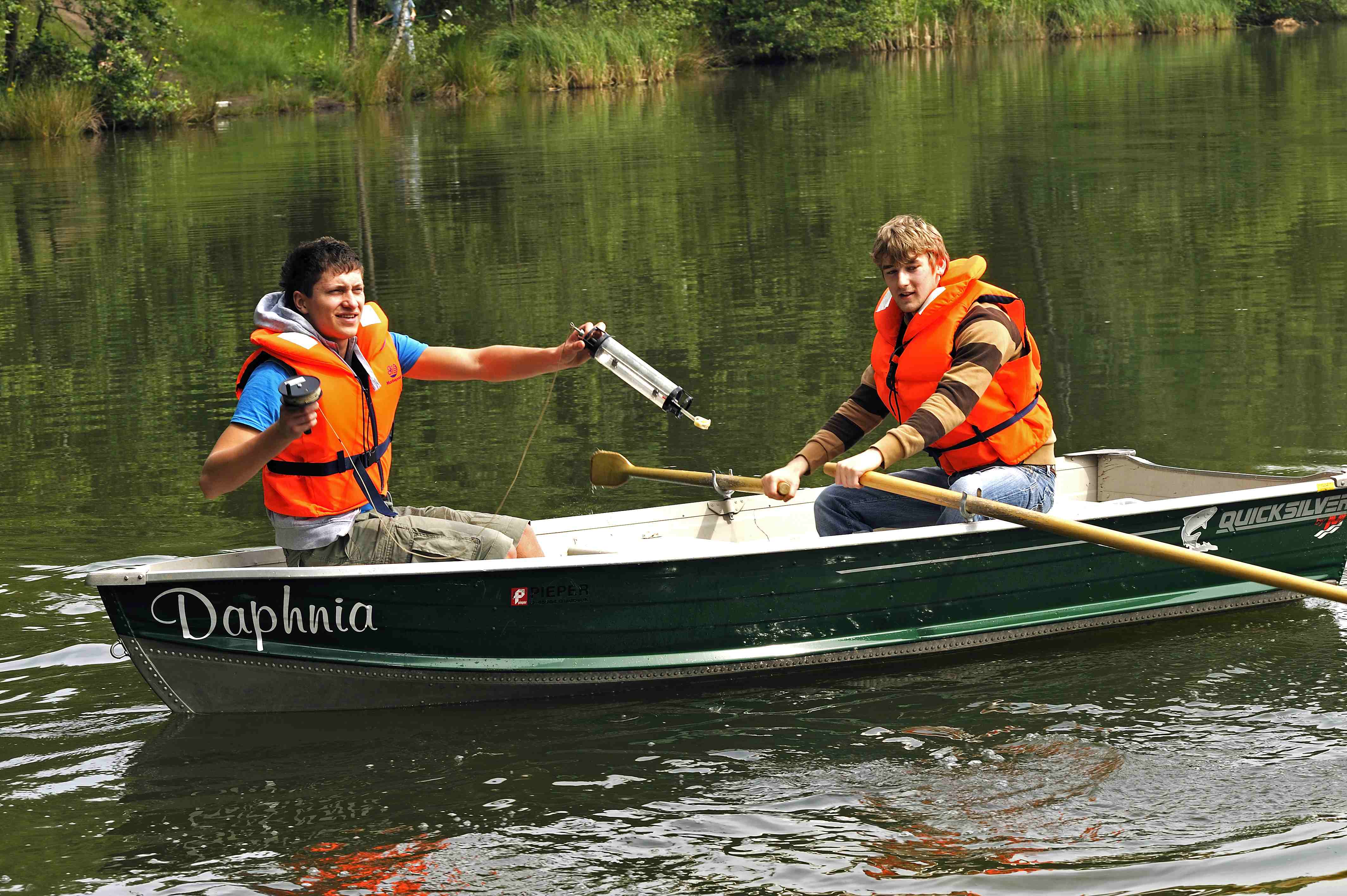 Zwei Jungen mit Wasserprobenbehälter in einem Boot