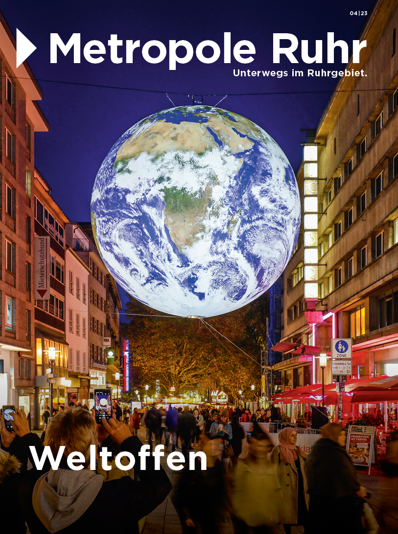 Cover der Dezemberausgabe: Es zeigt eine große Weltkugel, die inmitten einer Fußgängerzone schwebt. 
