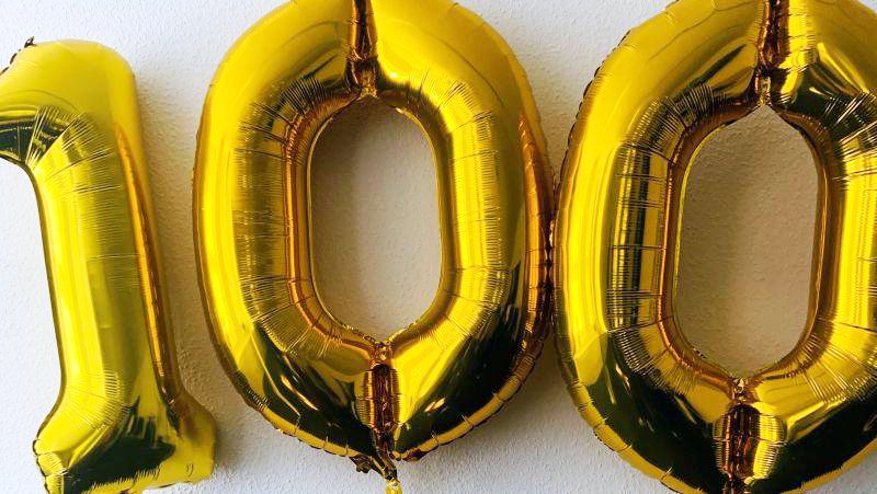drei goldene Luftballons bilden die Ziffer 100.