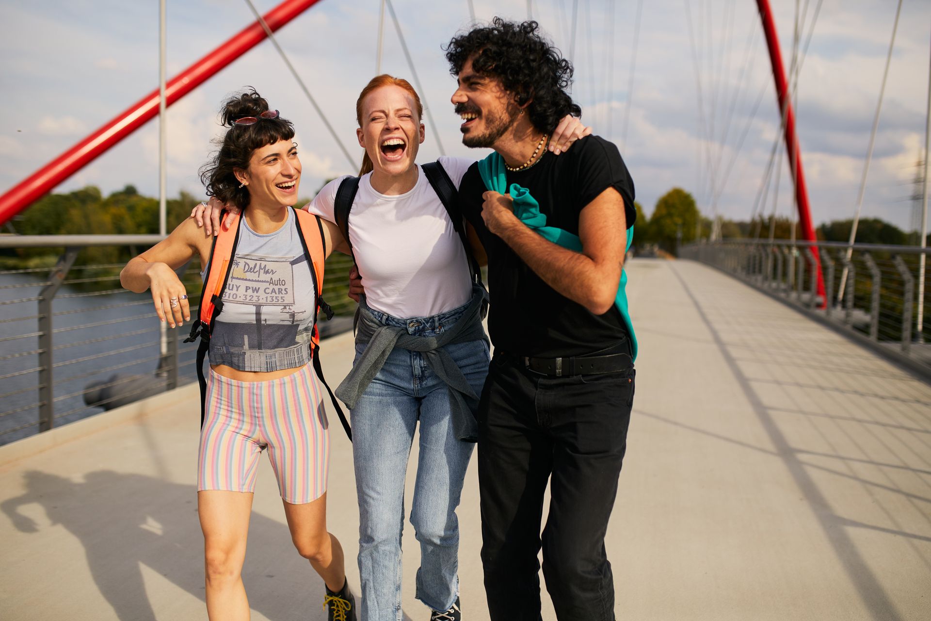 Drei Personen wandern über eine Brücke und lächeln freundlich dabei. 