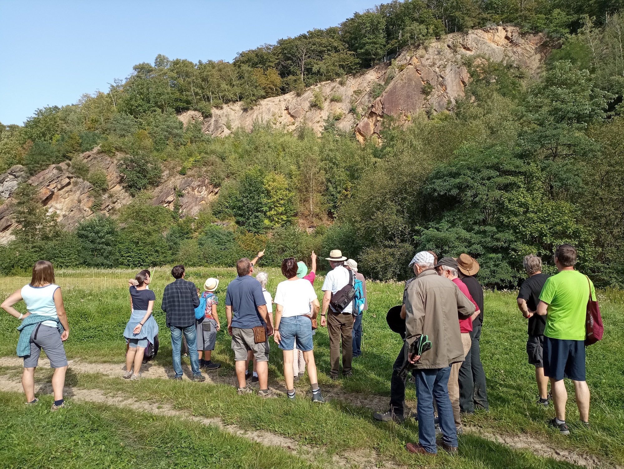 Eine Personengruppe steht vor einer Felswand. 