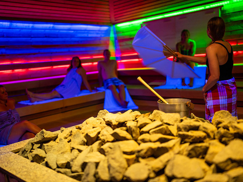 Personen sitzen in der Therme. Eine Person schwenkt mit einem Fächer.