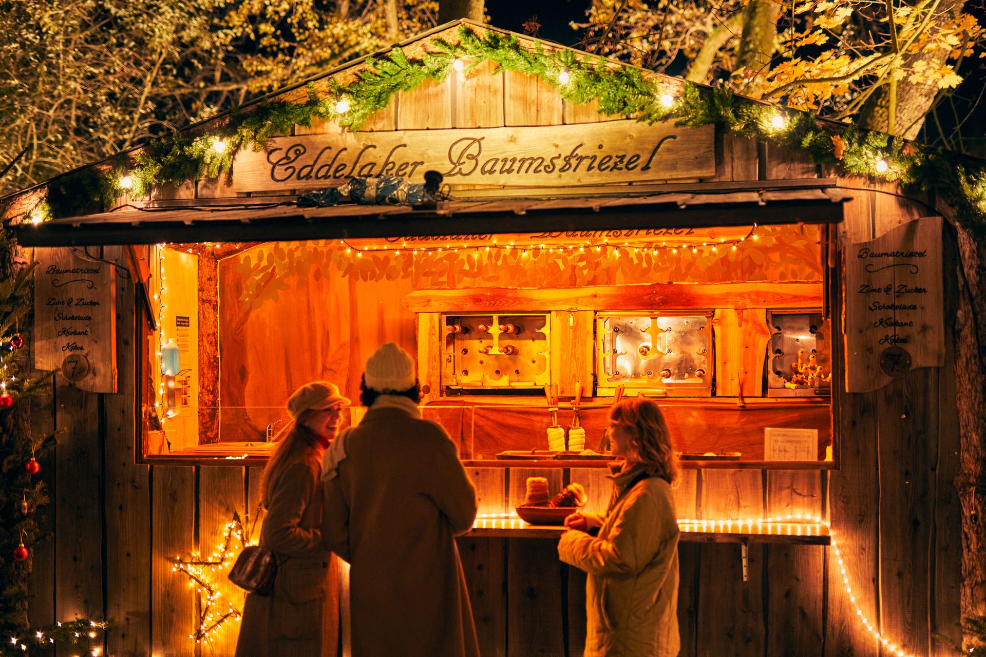 Drei Personen stehen vor einem Stand auf dem Weihnachtsmarkt.