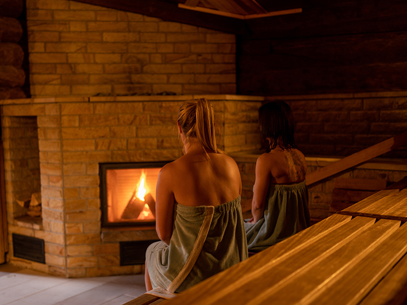 Zwei Personen sitzen in der Sauna vor einem Kamin.