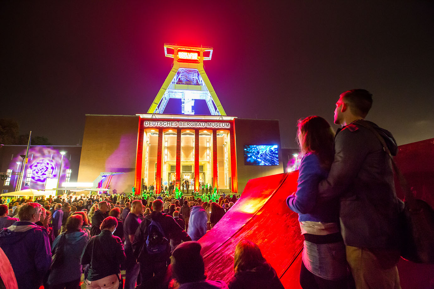 Leuchtender Förderturm. Davor eine große Menschenmenge.
