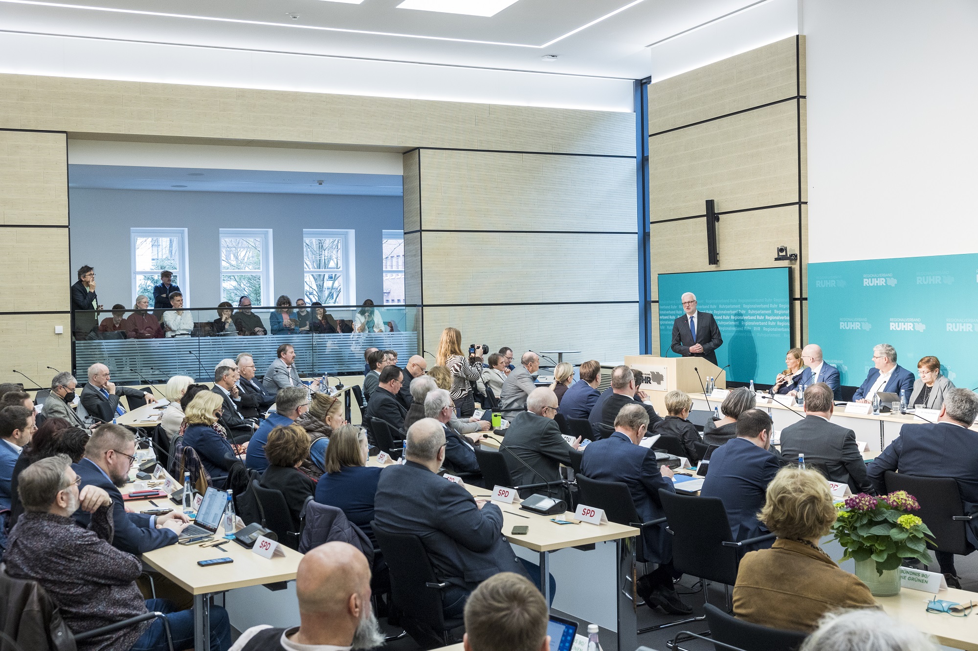 Menschen sitzen in einem vollen Sitzungsaal.
