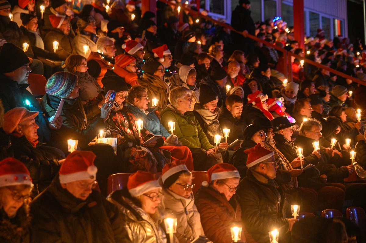Menschen singen gemeinsam auf einer Tribüne und halten Lichter in der Hand. 