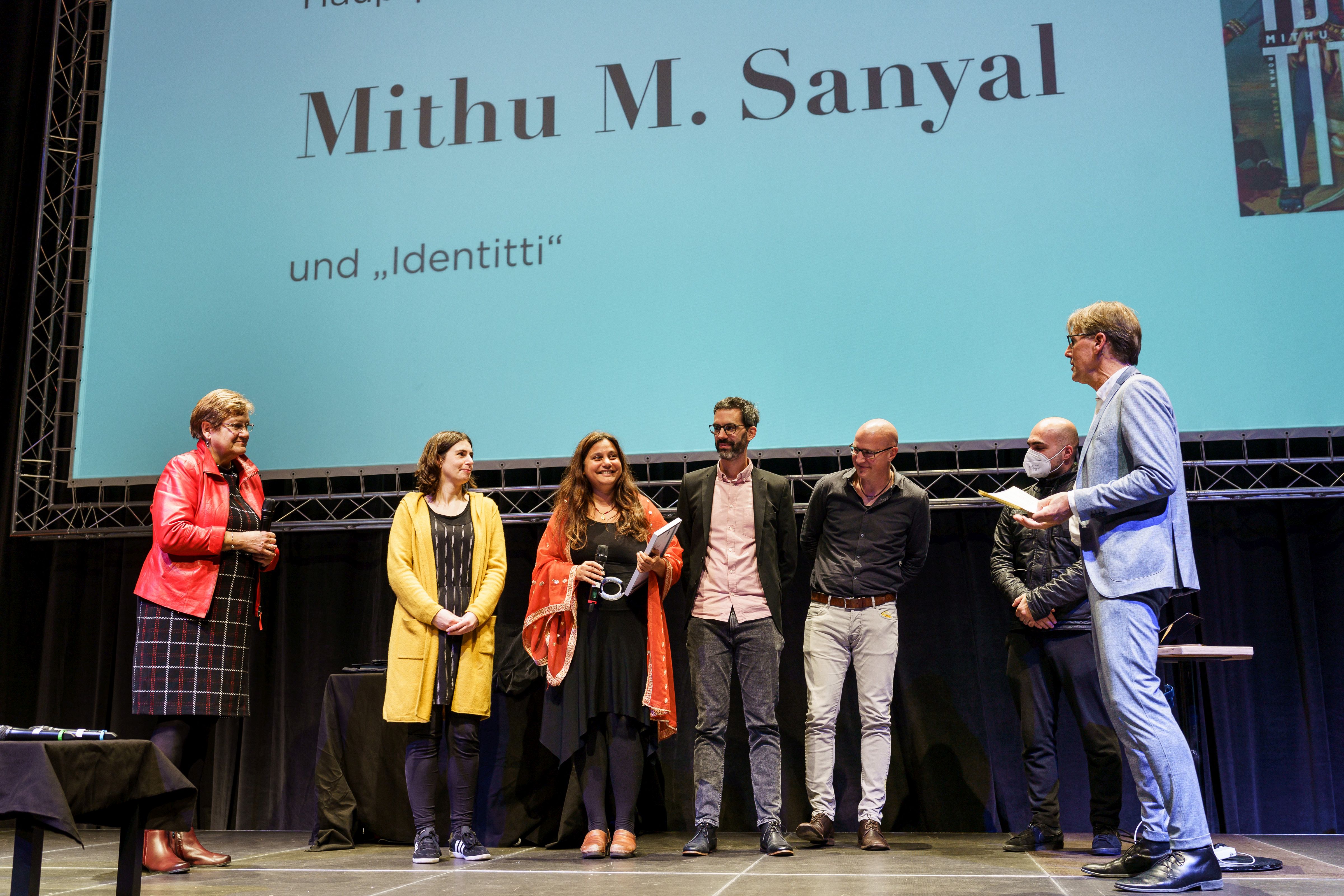 Hauptpreisträgerin Mithu M. Sanyal (Mitte) zusammen mit RVR-Regionaldirektorin Karola Geiß-Netthöfel (l.), Moderator Peter Großmann (r.) auf der Bühne im Ruhrfestspielhaus in Recklinghausen, begleitet von den weiteren Nominierten zum Hauptpreis des Literaturpreises Ruhr 2021.
