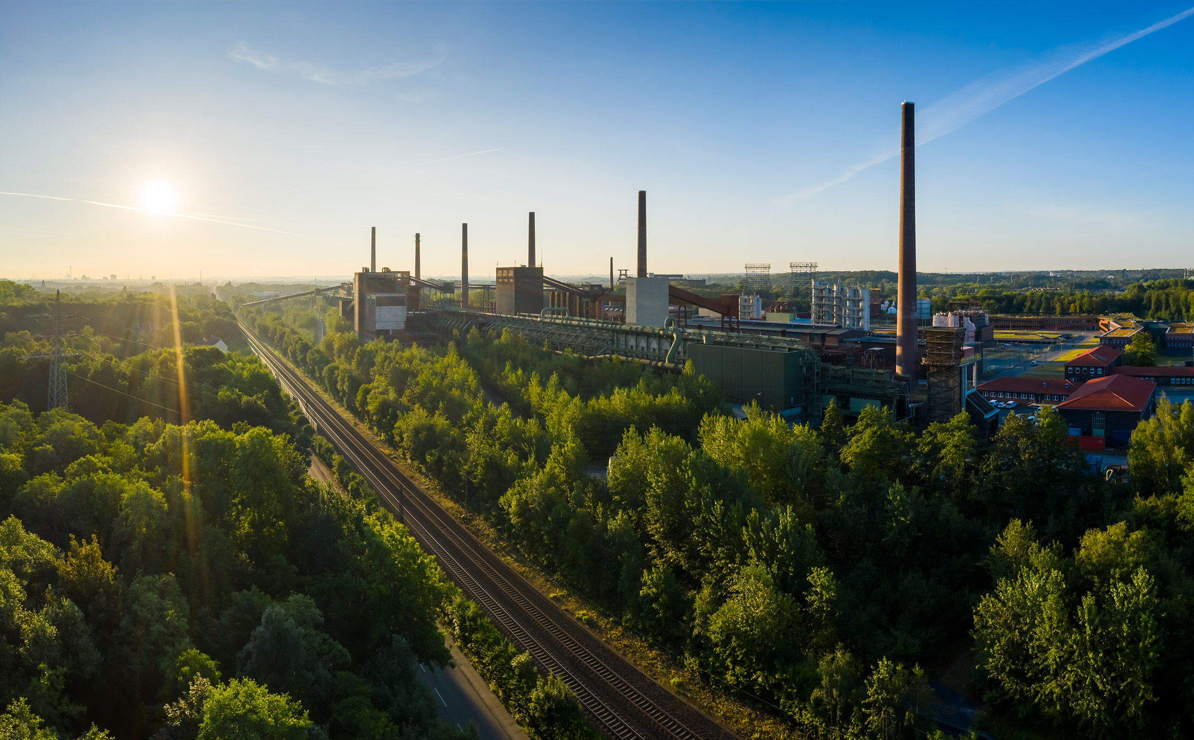 Blick über das grüne Ruhrgebiet und das Welterbe Zollverein mit der ehemaligen Kokerei im Vordergrund in Essen.