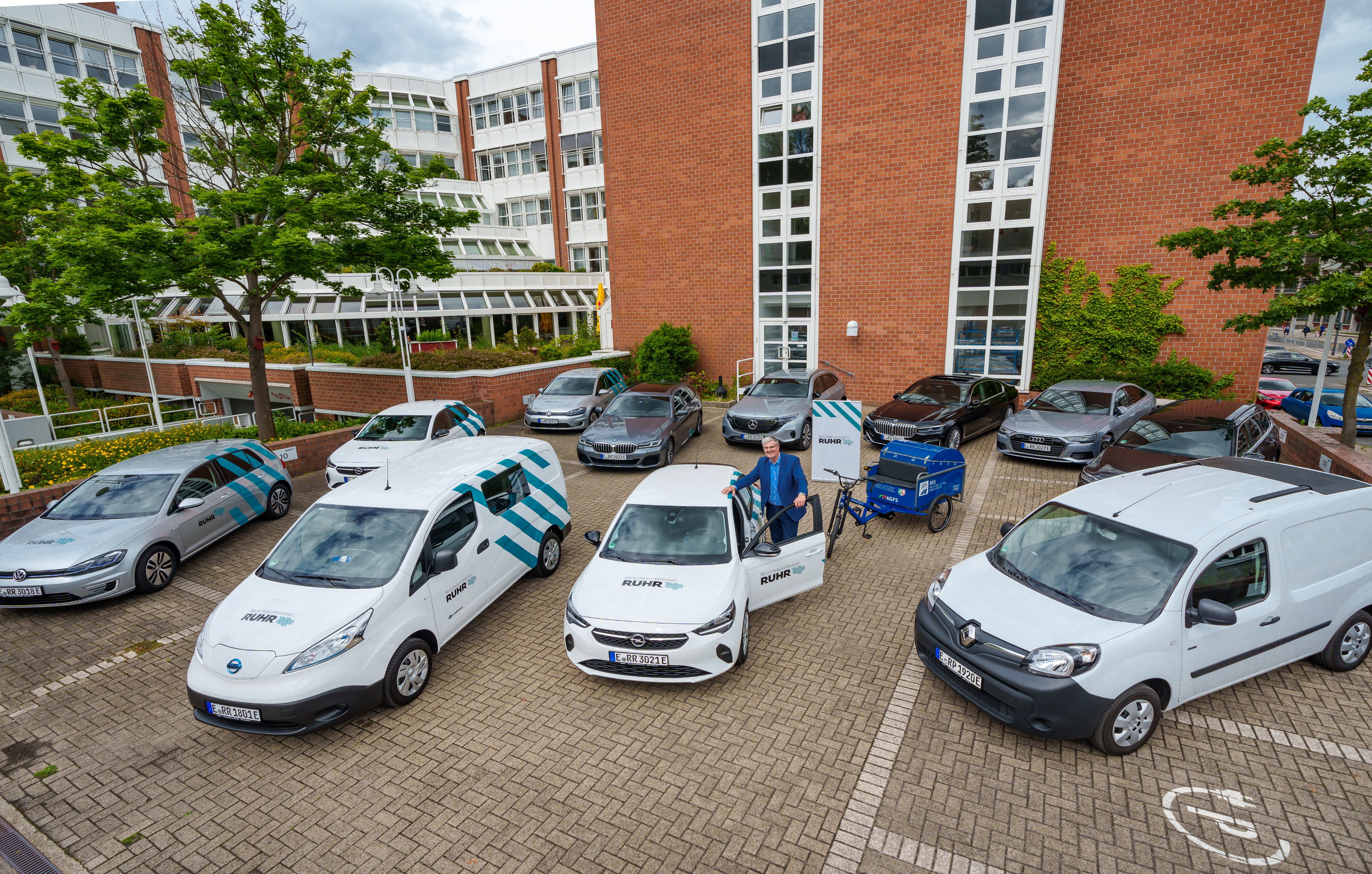 RVR-Parkplatz mit 6 E-Autos und 1 Lastenfahrrad. Im Vordergrund stehend der Dezernent für Wirtschaft.