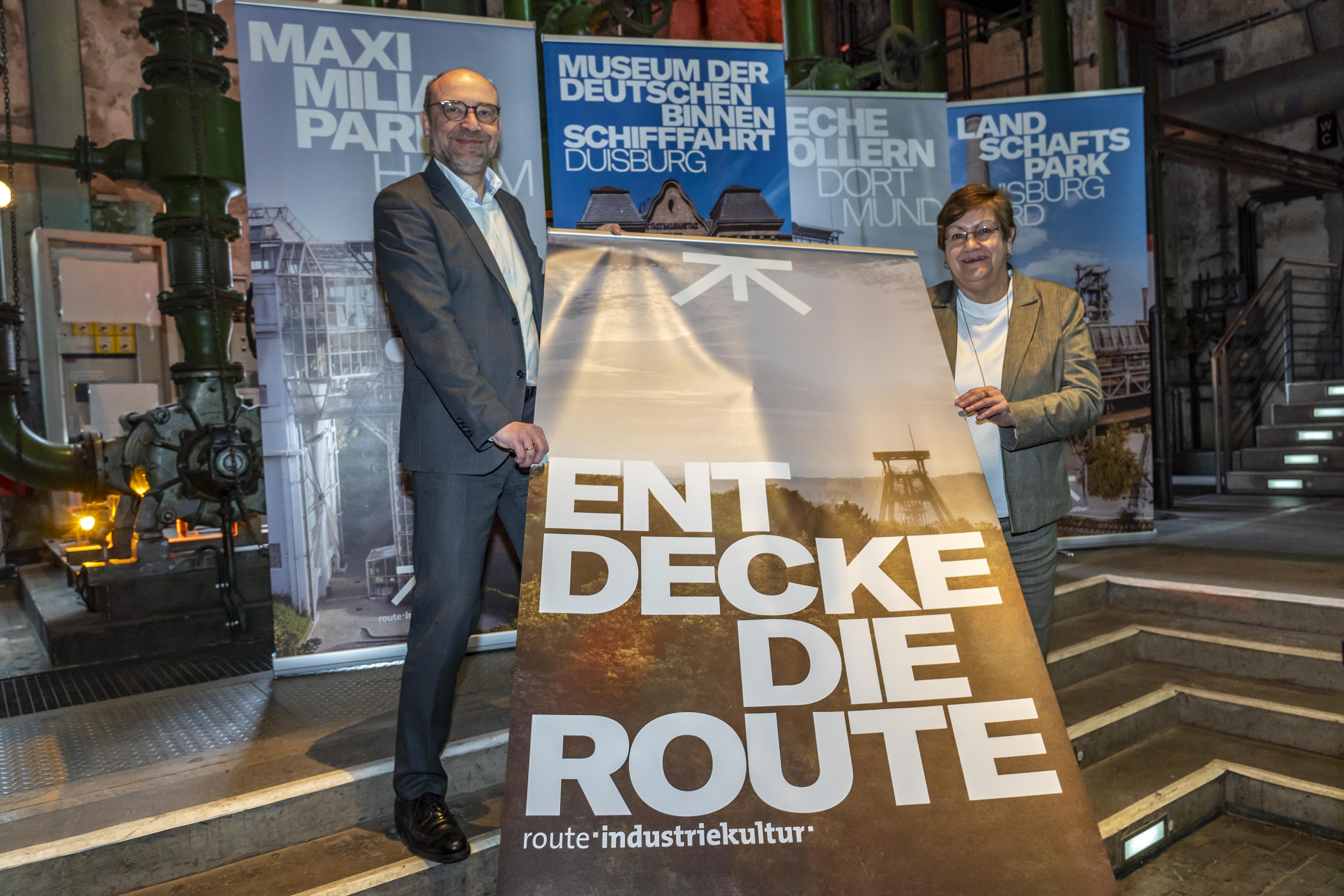 2 Personen halten Banner hoch mit Aufschrift "Entdecke die Route"