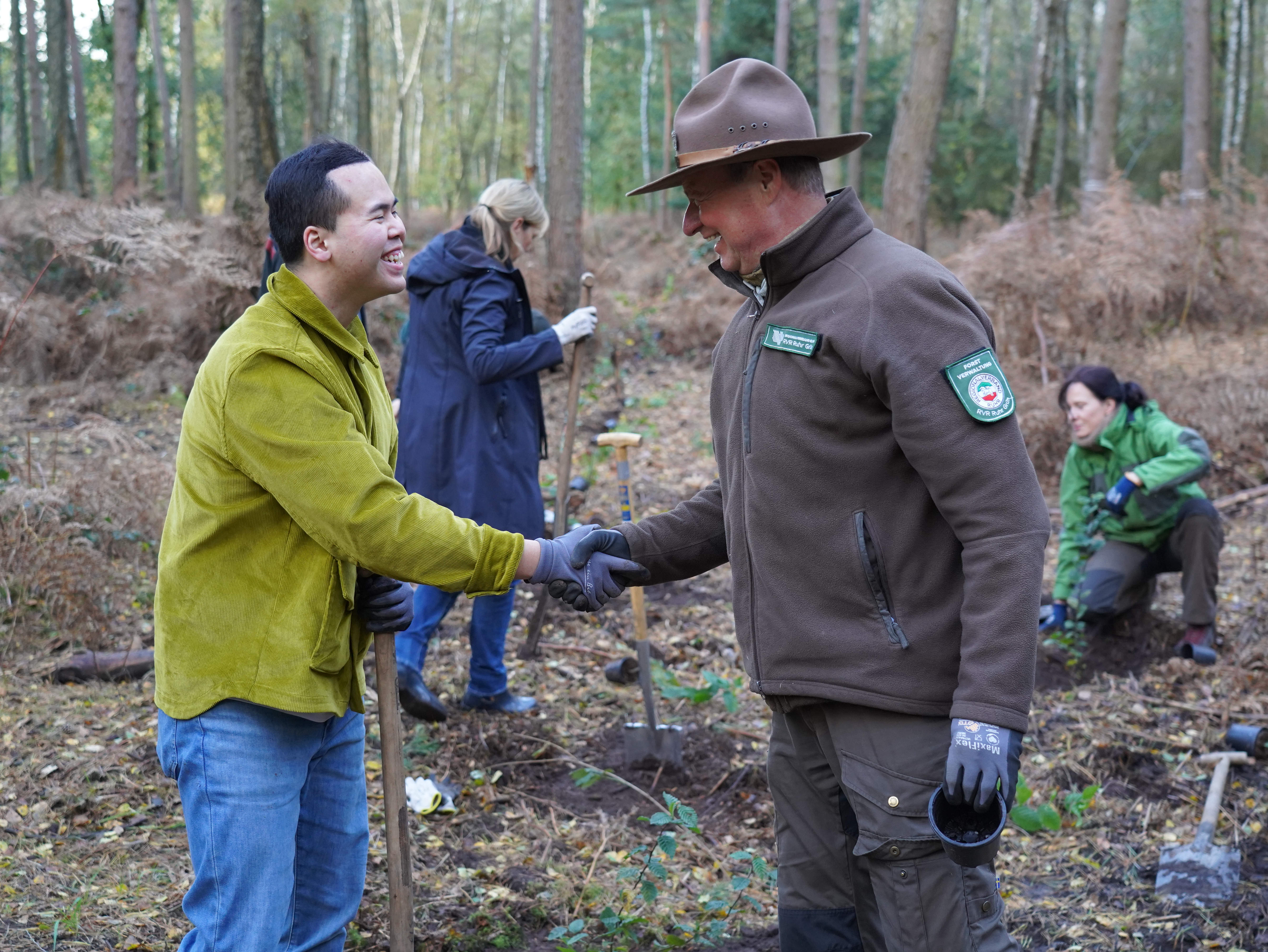 Zum Artikel Projekt „Unser Wald für Generationen.“, das Foto zeigt Long Do Hoang, Projekt Manager bei thyssenkrupp Schulte, und RVR-Ranger Jürgen Grewer. beim Handschlag im Wald.