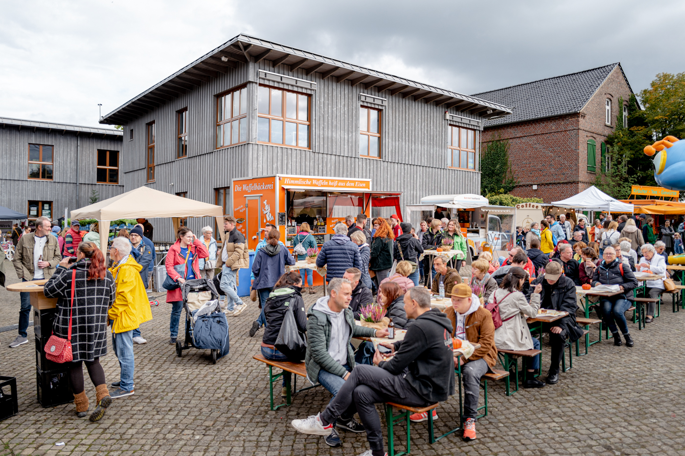 Menschen sitzen an mit Getränken und Speisen an Tischen vor dem Haus Ripshorst.