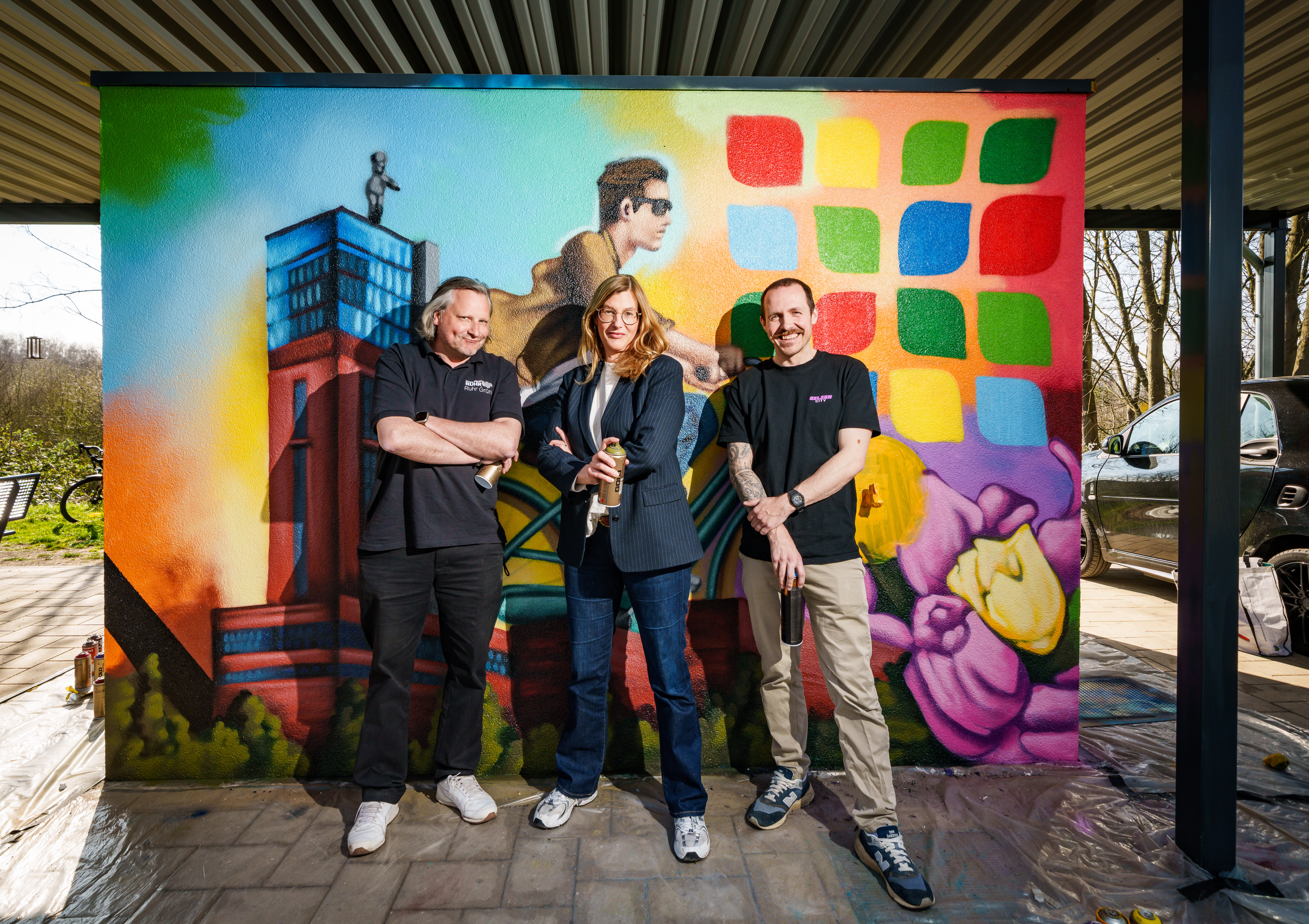 Drei Personen stehen vor einer bunten Graffiti-Wand