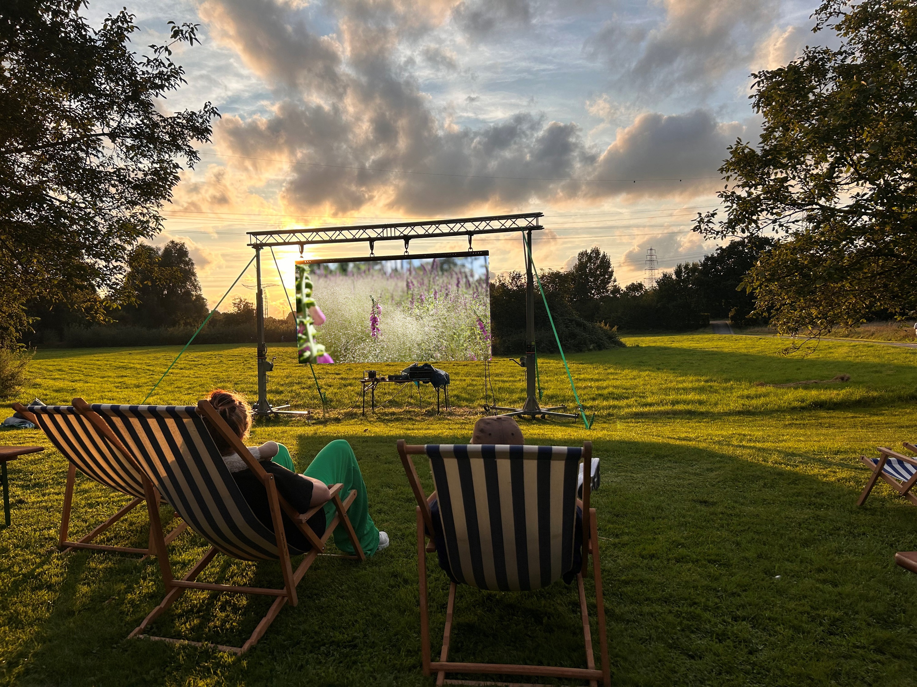Zwei Personen sitzen im Liegestuhl und gucken auf eine Leinwand von Natur umgeben.