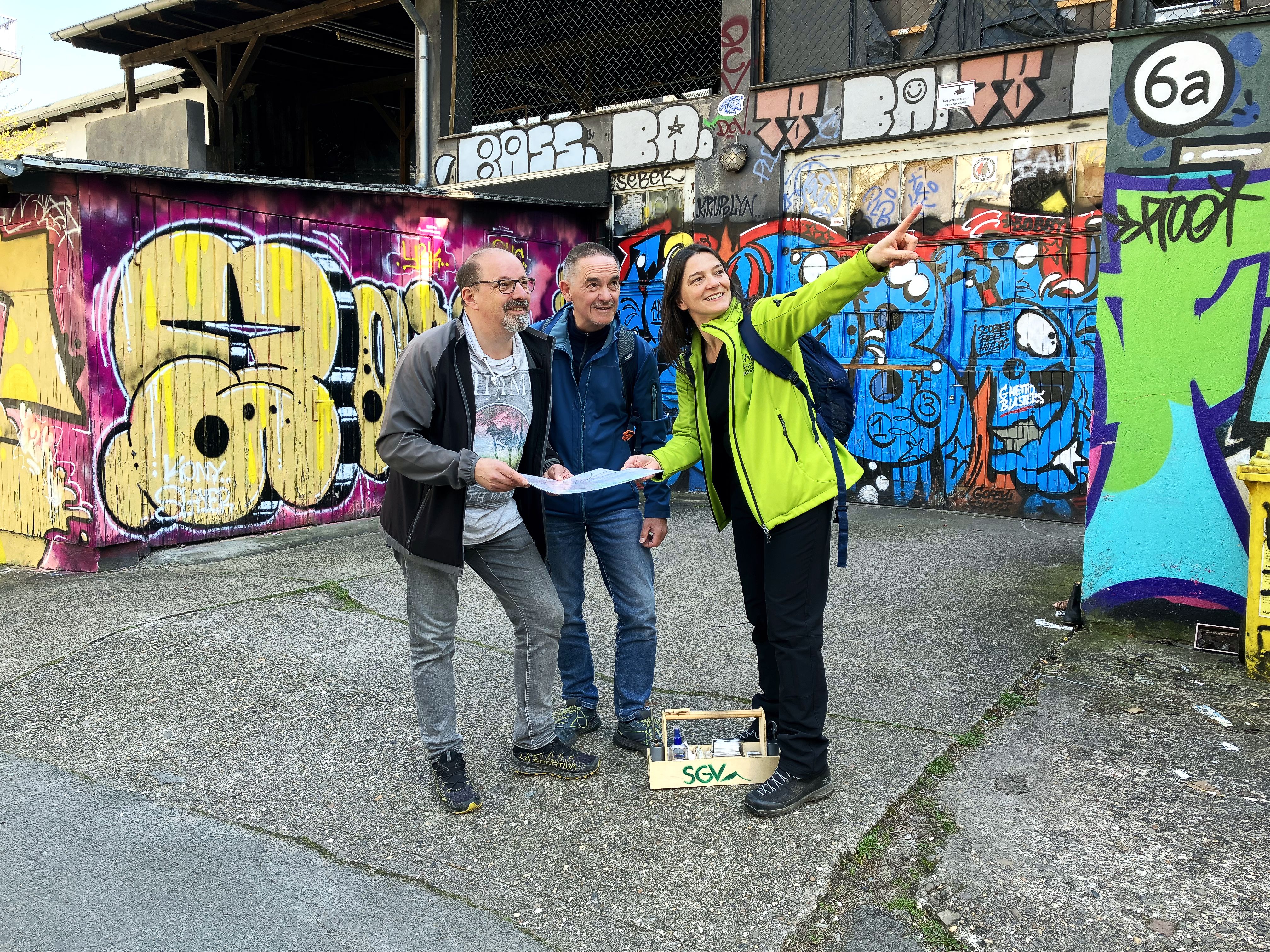 Drei Personen mit Stadtkarte in der Hand in einem Hinterhof. 