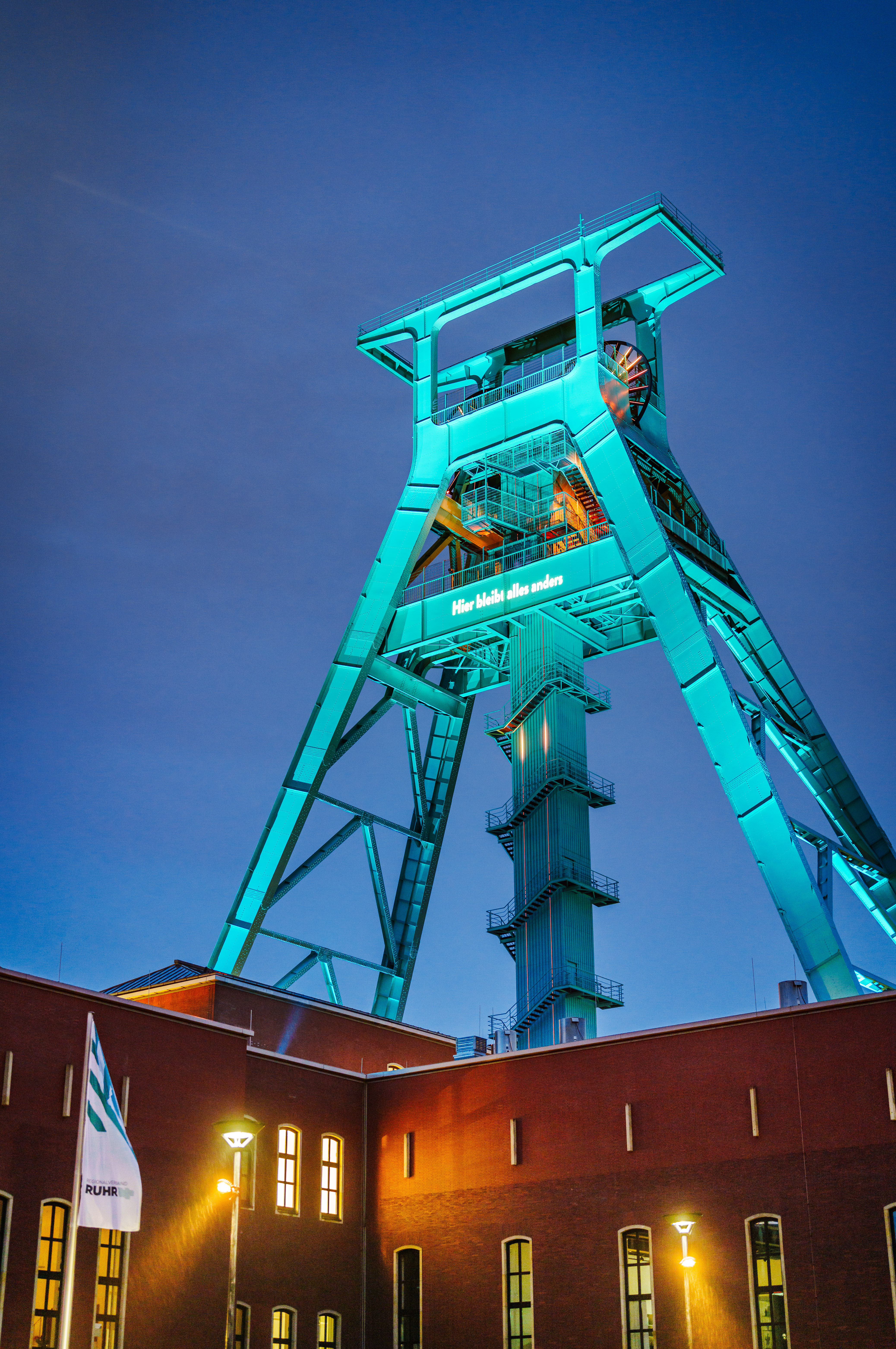 Der Förderturm am Bergbaumuseum Bochum strahlt in Petrolfarben. Gezeigt wird auch eine Aufschrift "Hierbleibt alles anders".