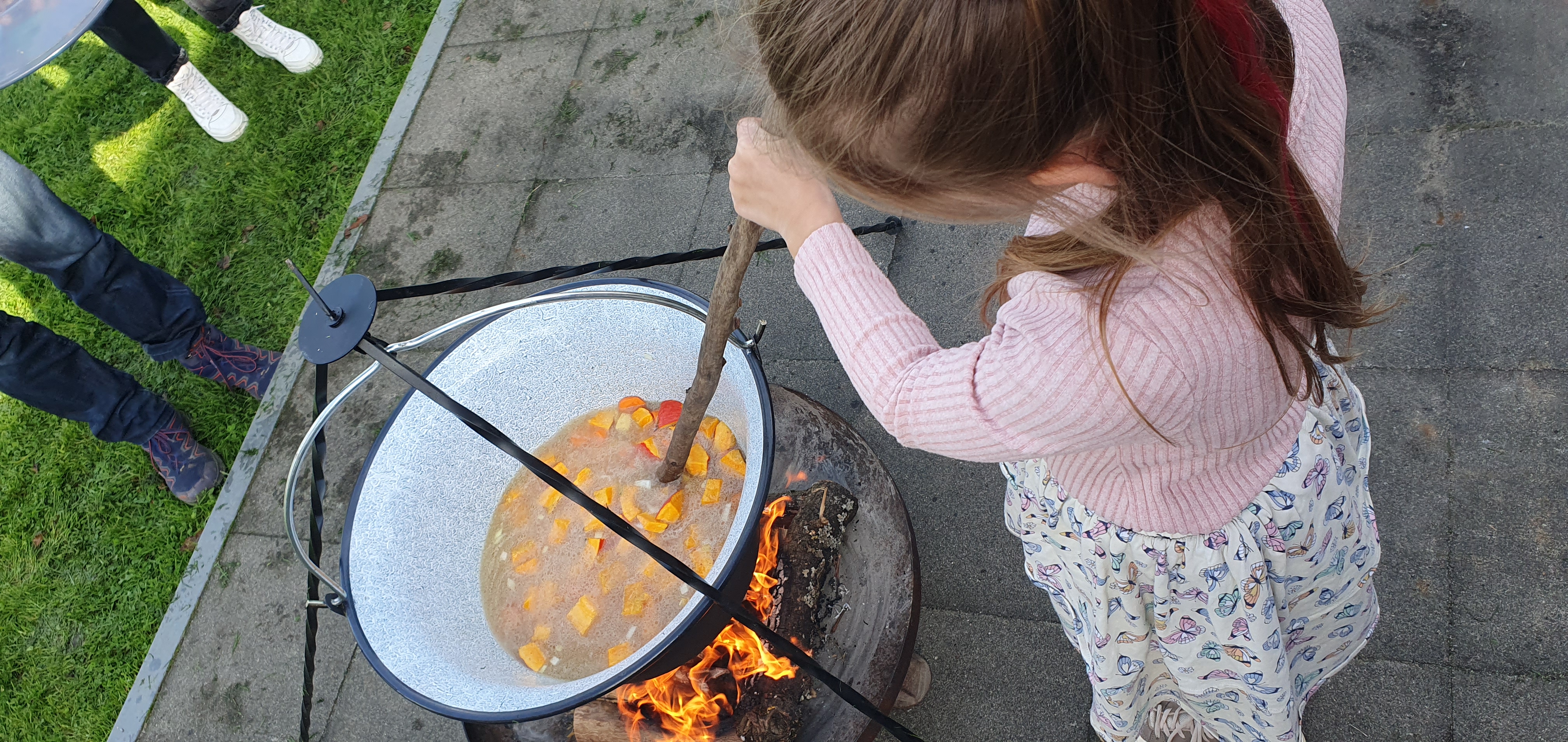 Ein Mädchen rührt in einem großen Topf mit Essen über dem Koffer