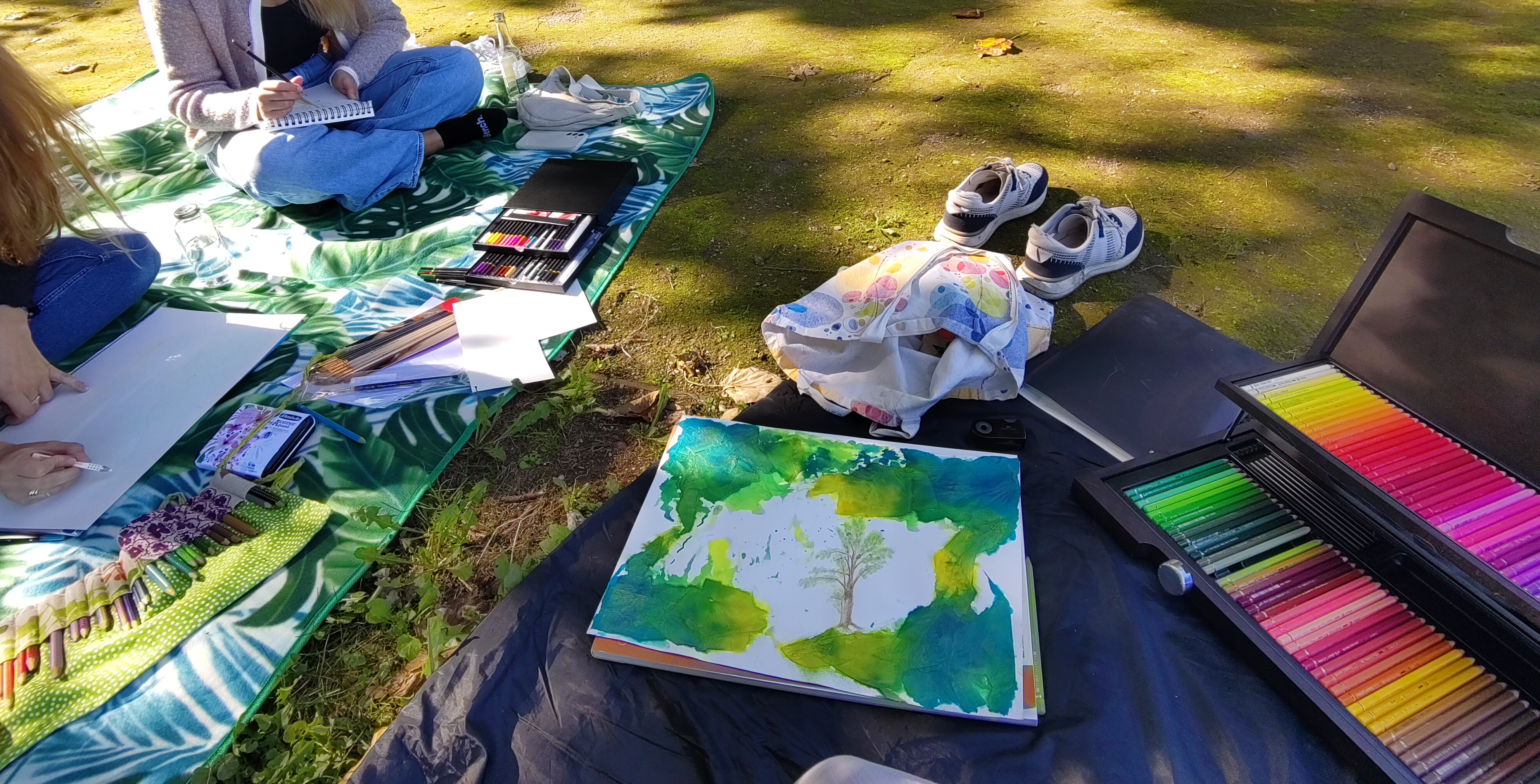 Es wird draußen auf einer Picknickdecke mit bunten Farben gemalt.