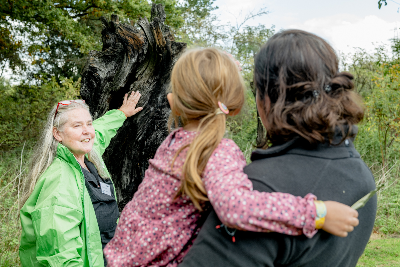 Eine Frau zeigt auf einen Baum. Zwei Personen schauen zu.