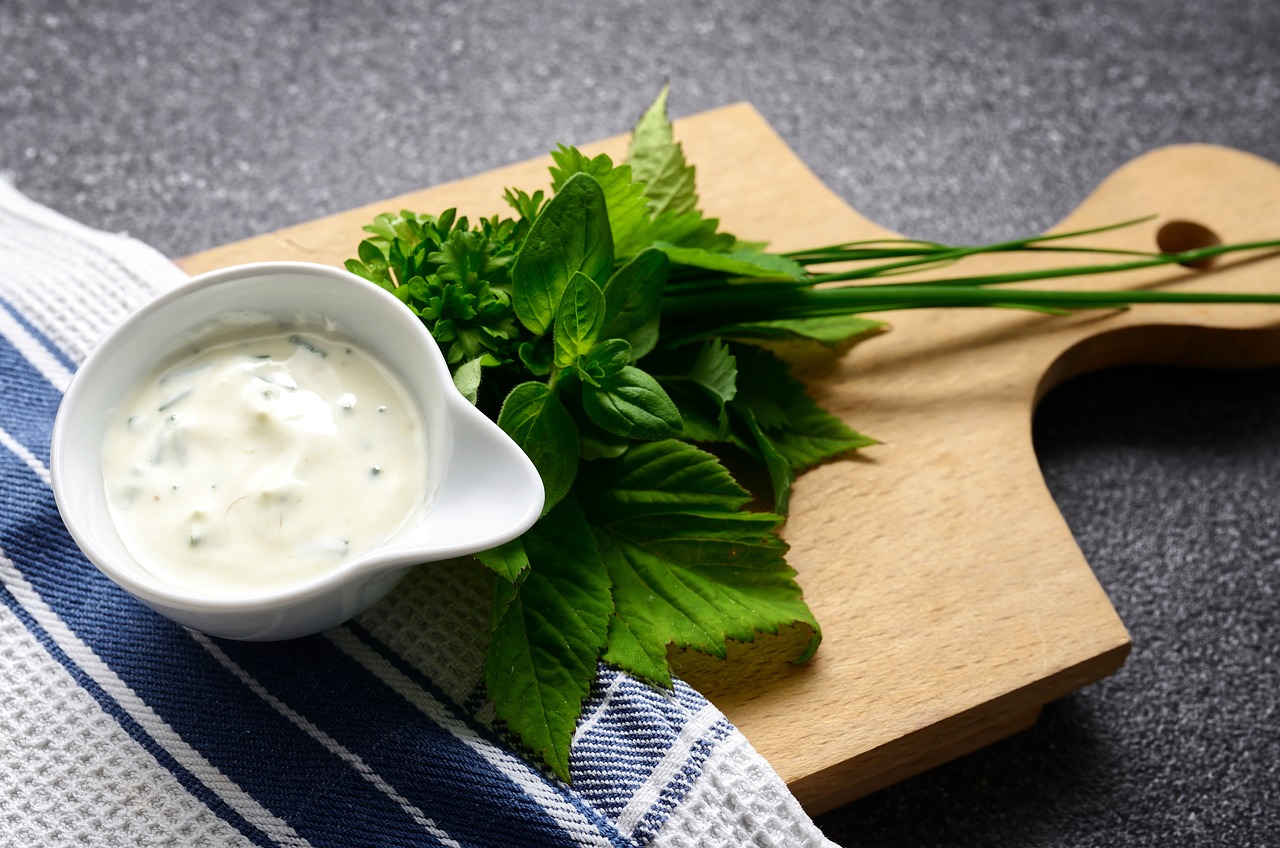 Eine Schüssel gefüllt mit Salatdressing, daneben liegen Kräuter. Beides wurde auf einem Holzbrett angerichtet.